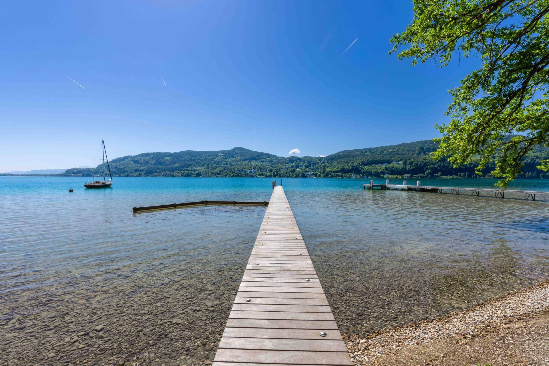 Langer Holzsteg führt ins klare, türkisfarbene Wasser des Sees, umgeben von grünen Hügeln.
