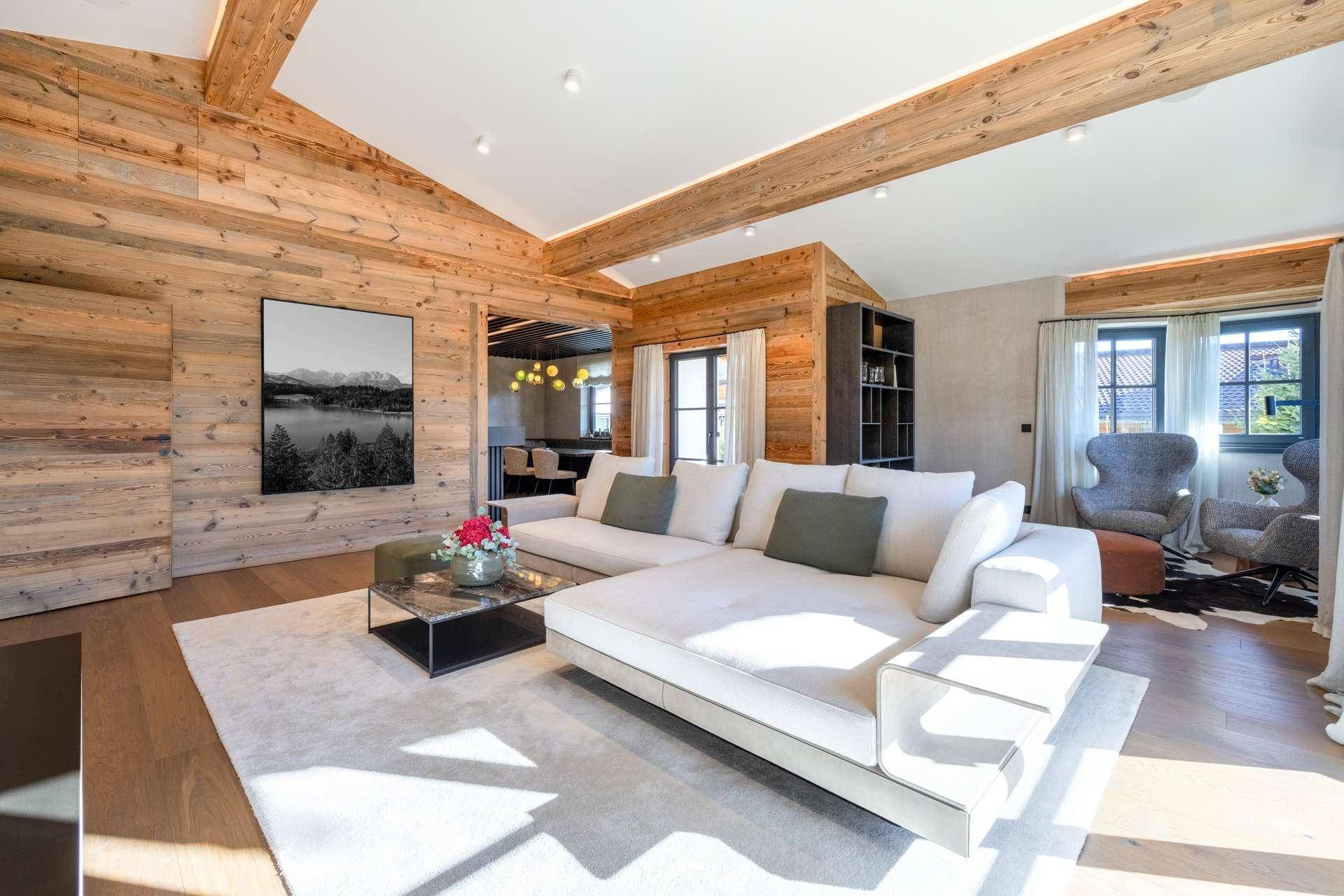 Helles Wohnzimmer mit bequemer Couch, Holzbalken und Blick auf die umliegende Landschaft.