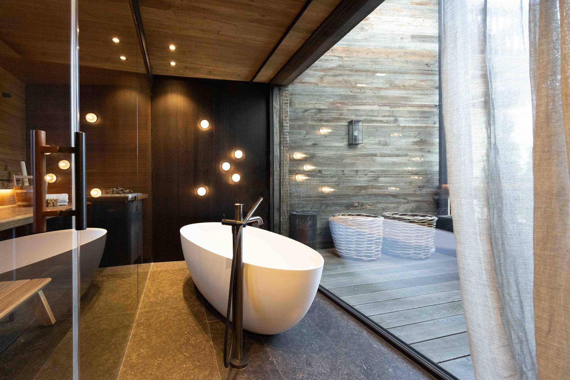 Luxuriöses Badezimmer mit freistehender Badewanne, Steinfliesen und direktem Zugang zu einem Holzdeck im Freien.