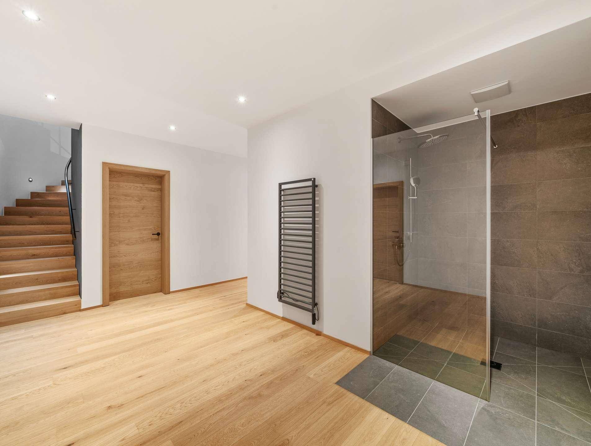Heller Flurbereich mit Holztreppe, moderner Duschkabine und beheiztem Handtuchhalter an der Wand.