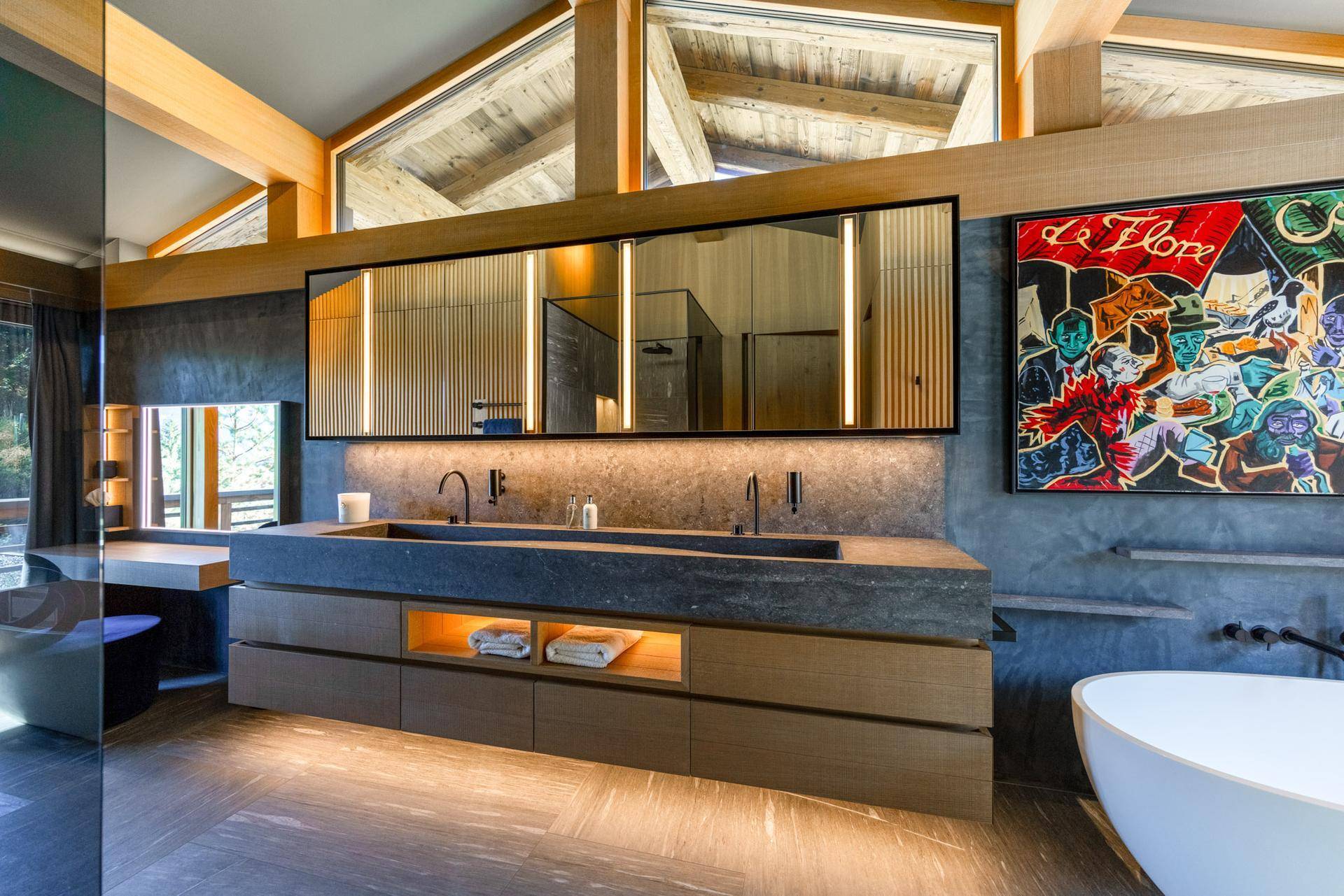 Luxuriöses Badezimmer mit Doppelwaschbecken, freistehender Badewanne und Holzbalken unter großen Fenstern.