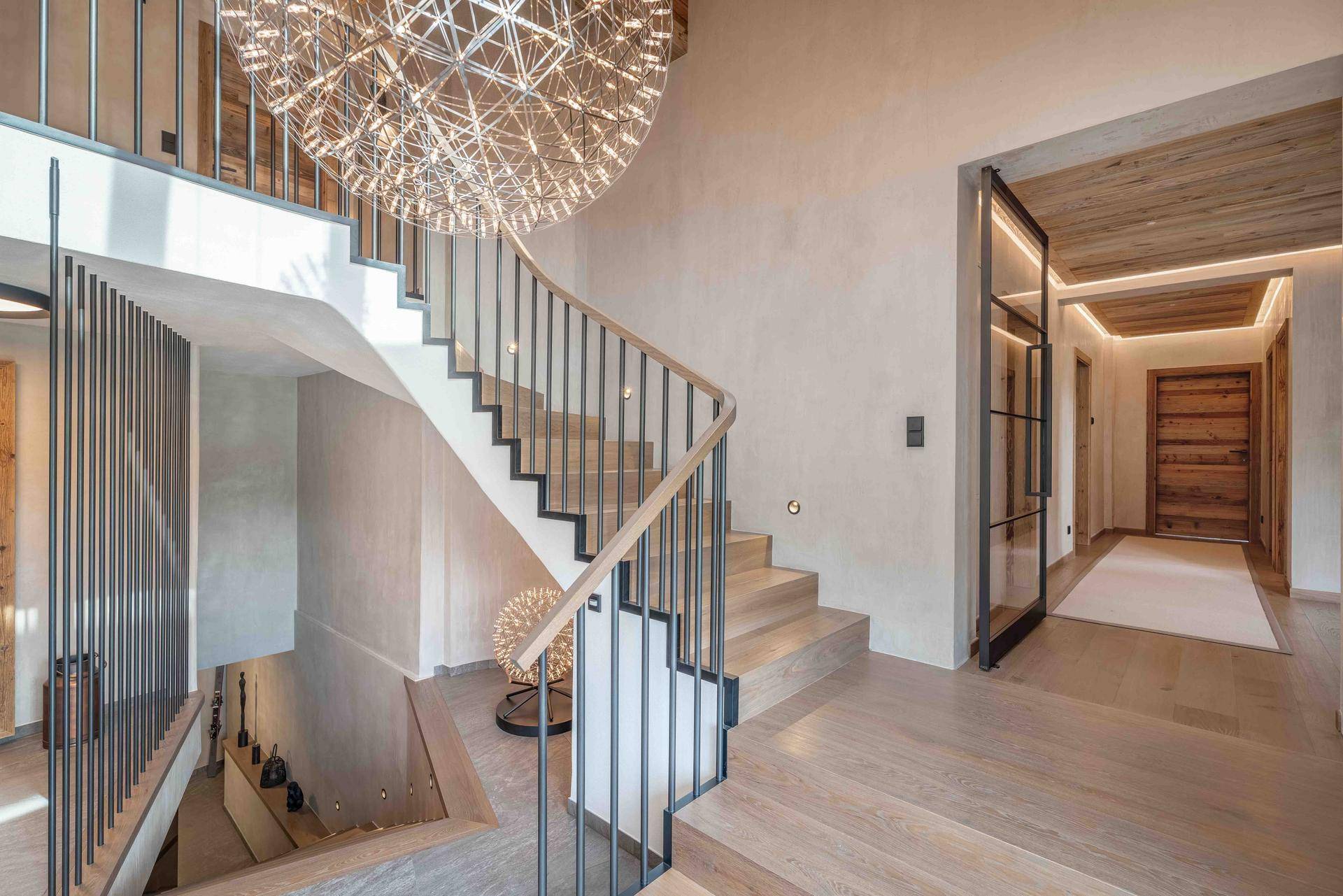 Heller Eingangsbereich mit moderner Treppe, Holzboden und großer Pendelleuchte.