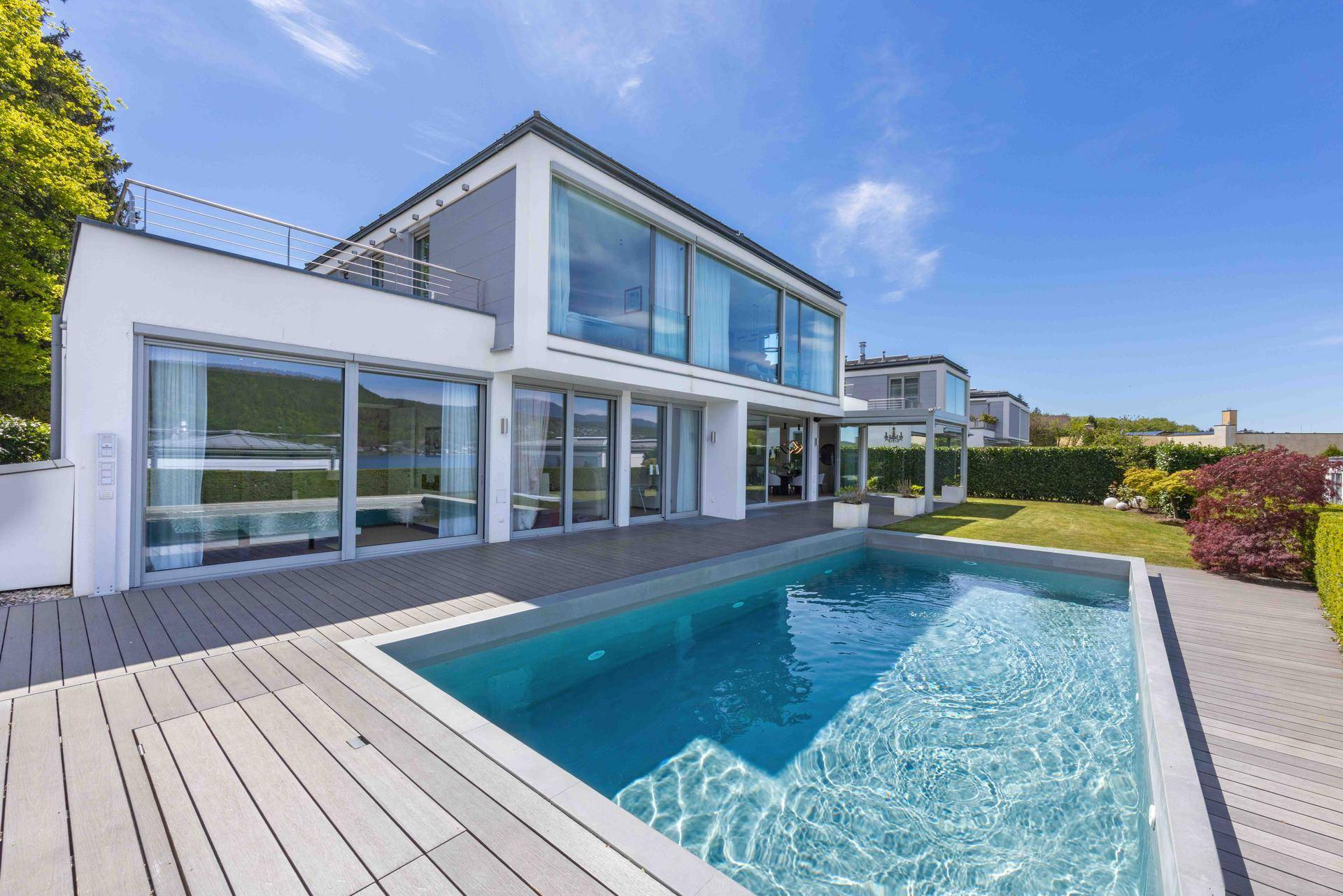 Moderne Villa mit großzügigem Poolbereich und Holzterrasse unter blauem Himmel.