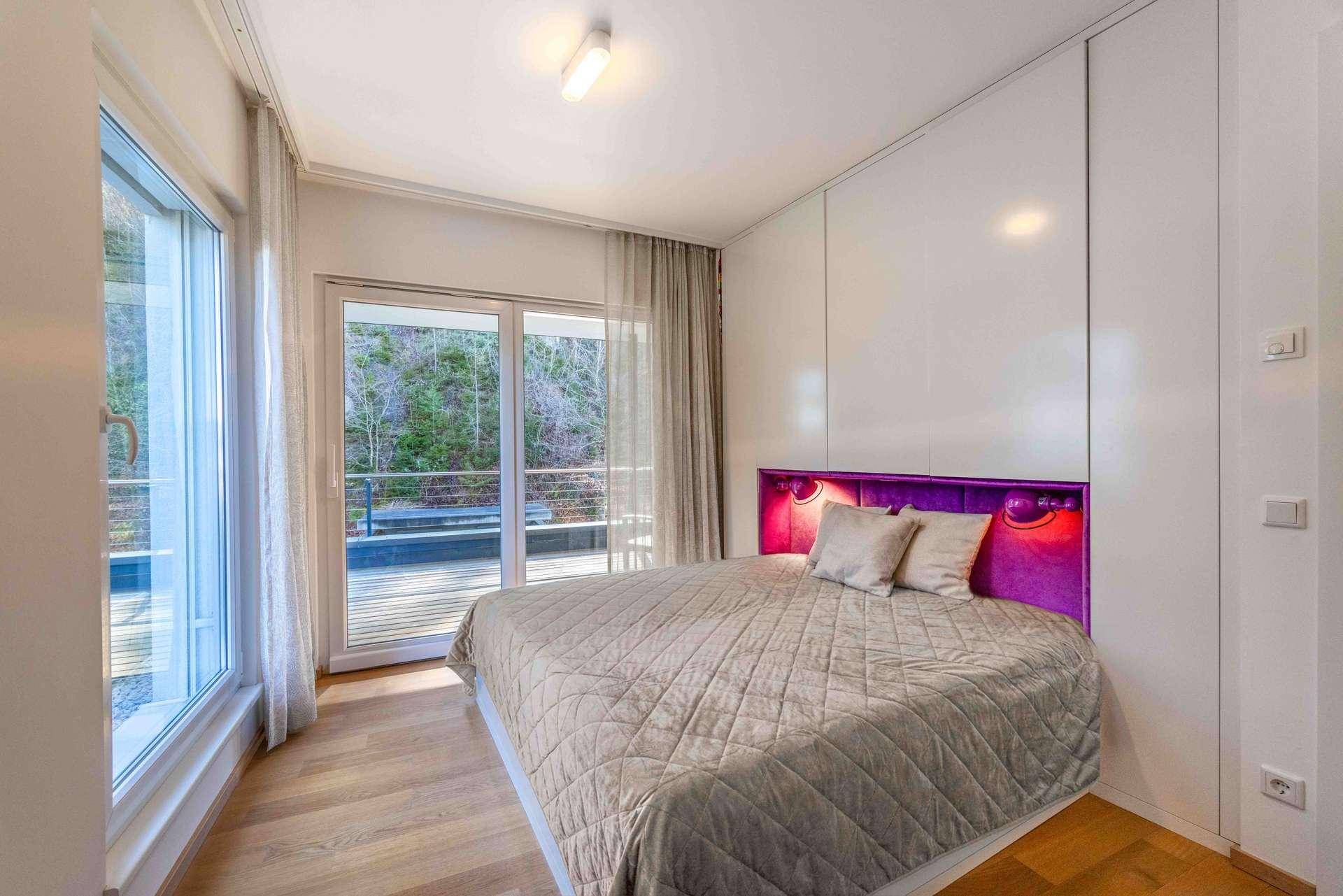 Gemütliches Schlafzimmer mit lila Kopfteil, Holzboden und Zugang zu einem Außenbereich.