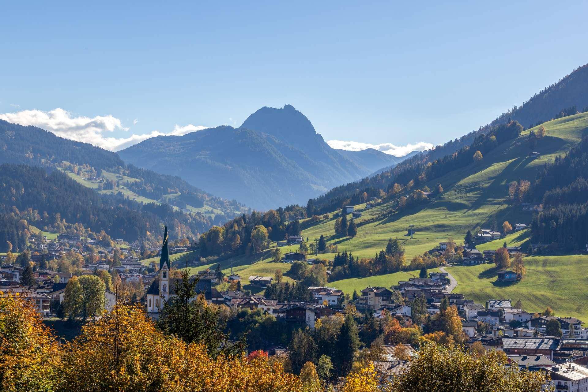 Malerische Berglandschaft mit einem charmanten Dorf im Tal, umgeben von grünen Hügeln und herbstlichen Bäumen.