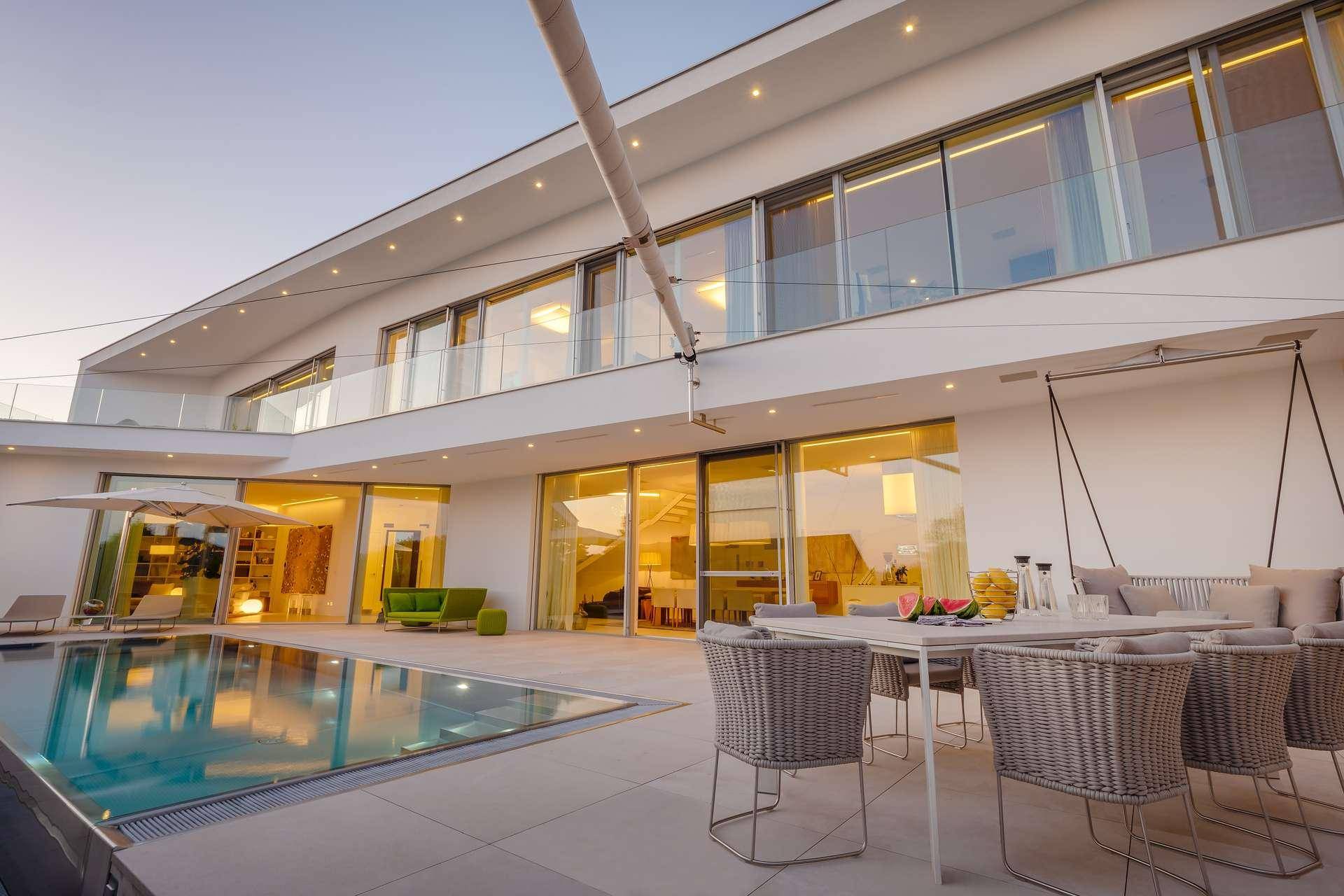 Abendliche Ansicht der modernen Villa mit beleuchtetem Pool und einladendem Essbereich im Freien.