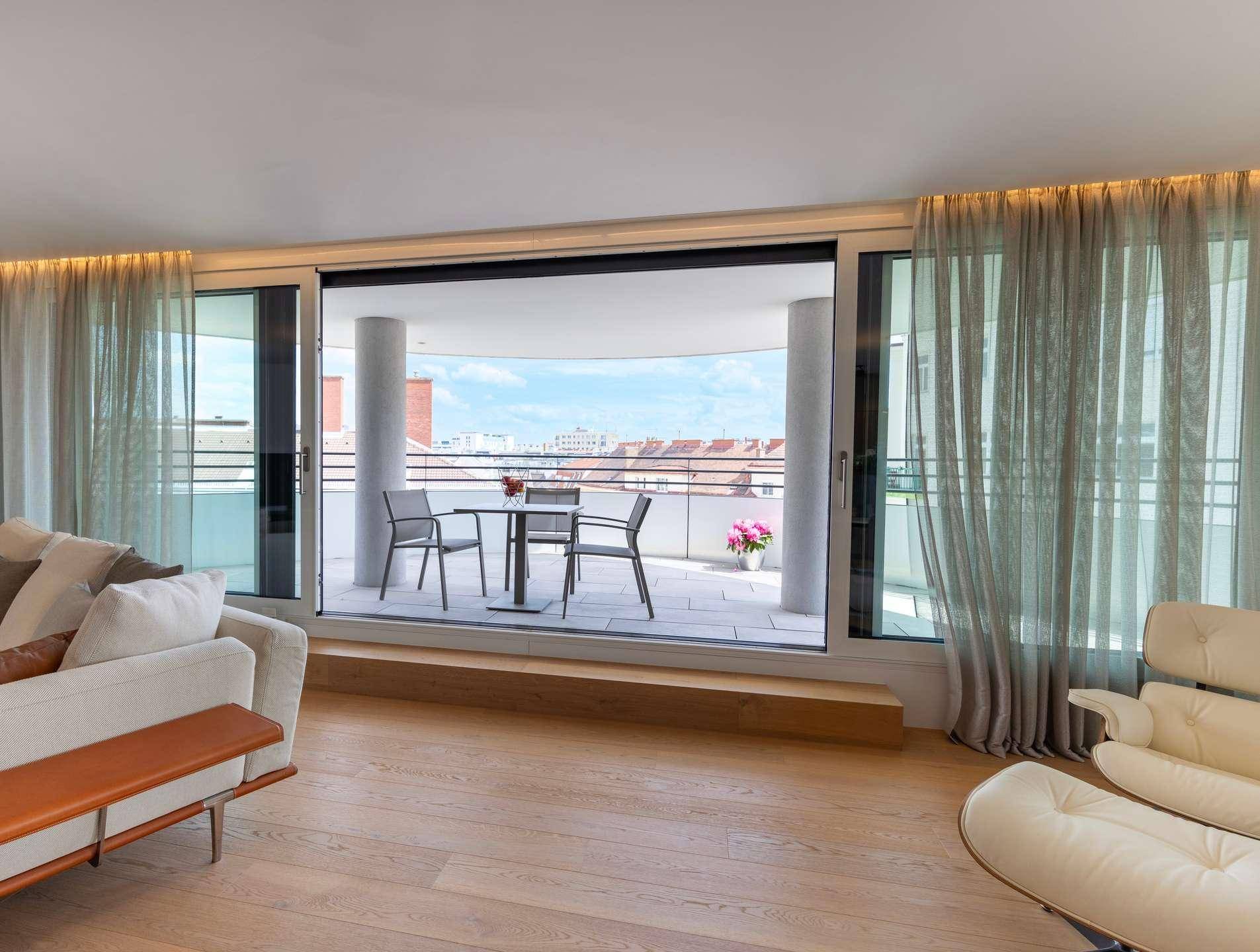 Helles Wohnzimmer mit Holzboden und großem Zugang zu einem möblierten Balkon mit Stadtblick.