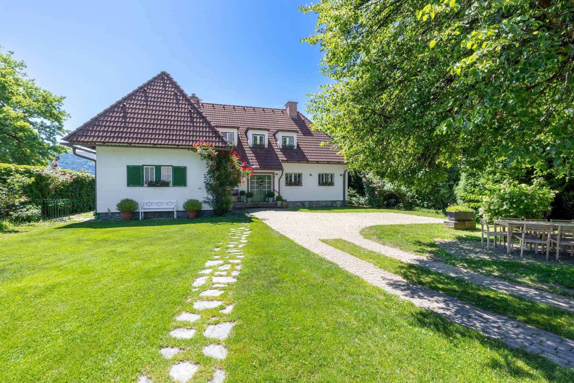Charmantes Landhaus mit großem Vorgarten, gepflegtem Rasen und traditioneller Architektur unter blauem Himmel.