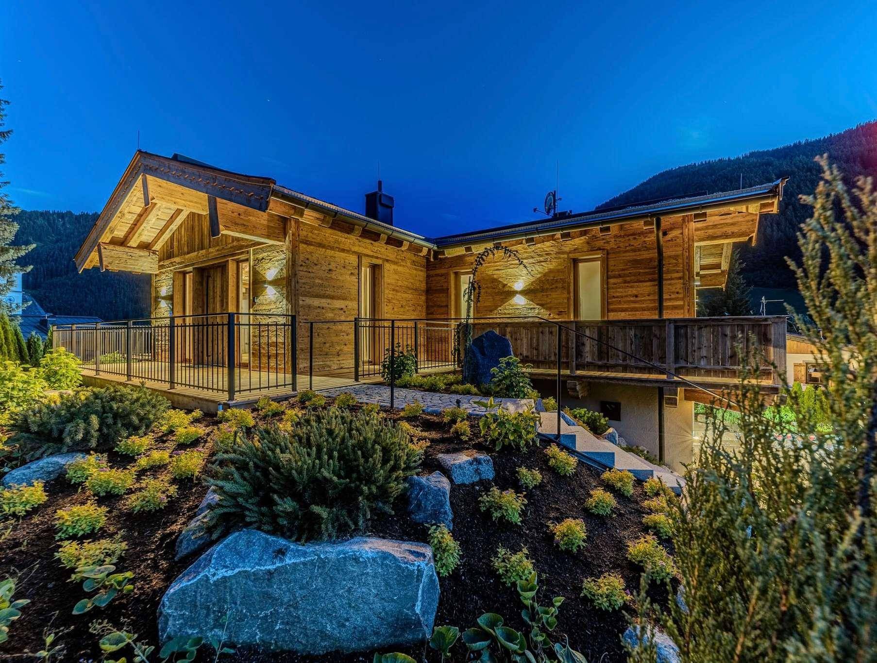 Charmantes Holzchalet mit gepflegtem Garten und beleuchteter Außenanlage bei Dämmerung.