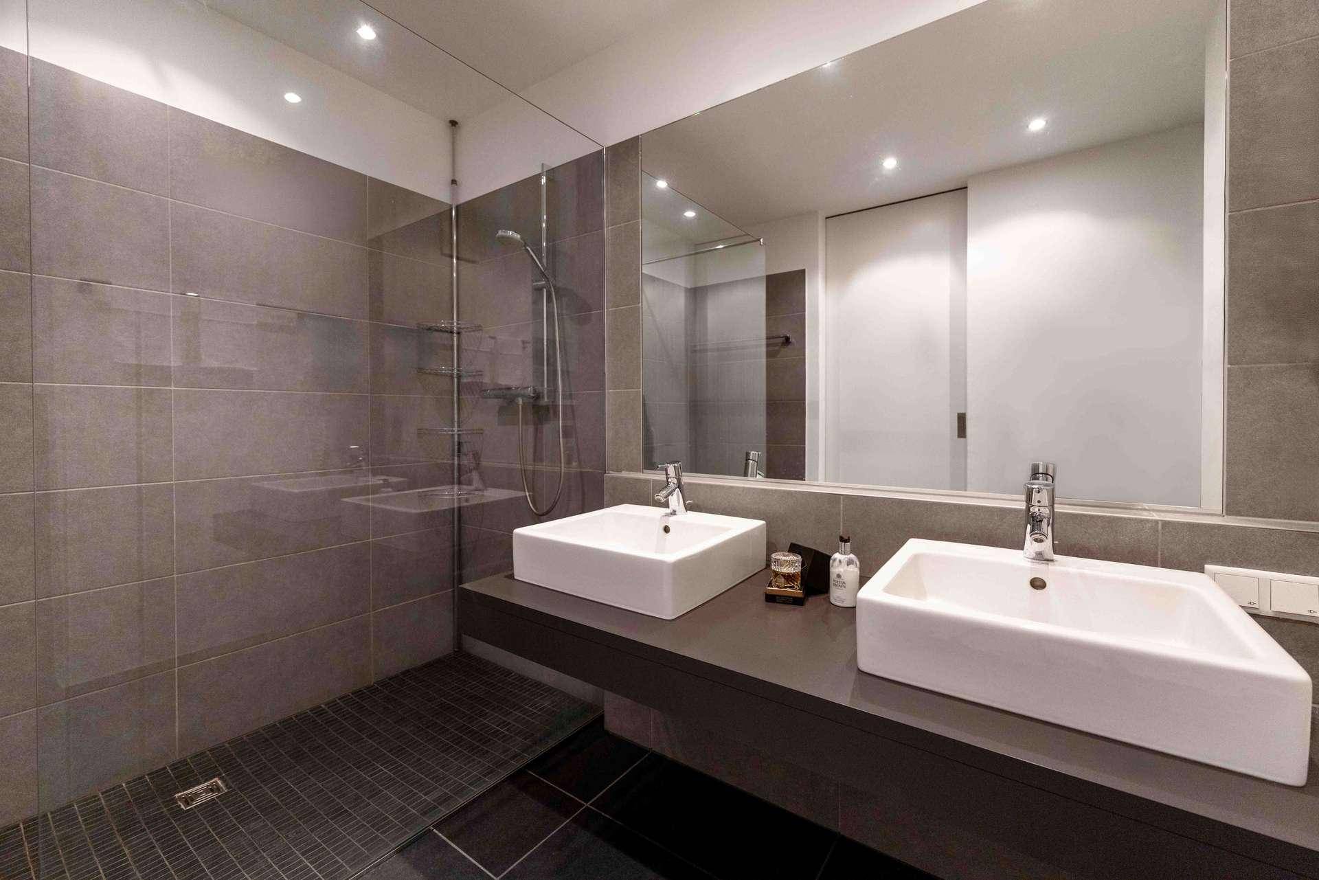Modernes Badezimmer mit grauen Fliesen, Doppelwaschbecken und einer begehbaren Dusche.