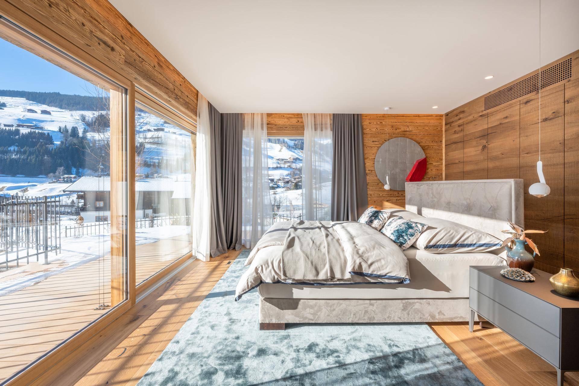 Lichtdurchflutetes Schlafzimmer mit Holzboden und Panoramafenstern, die den Blick auf die verschneite Landschaft freigeben.
