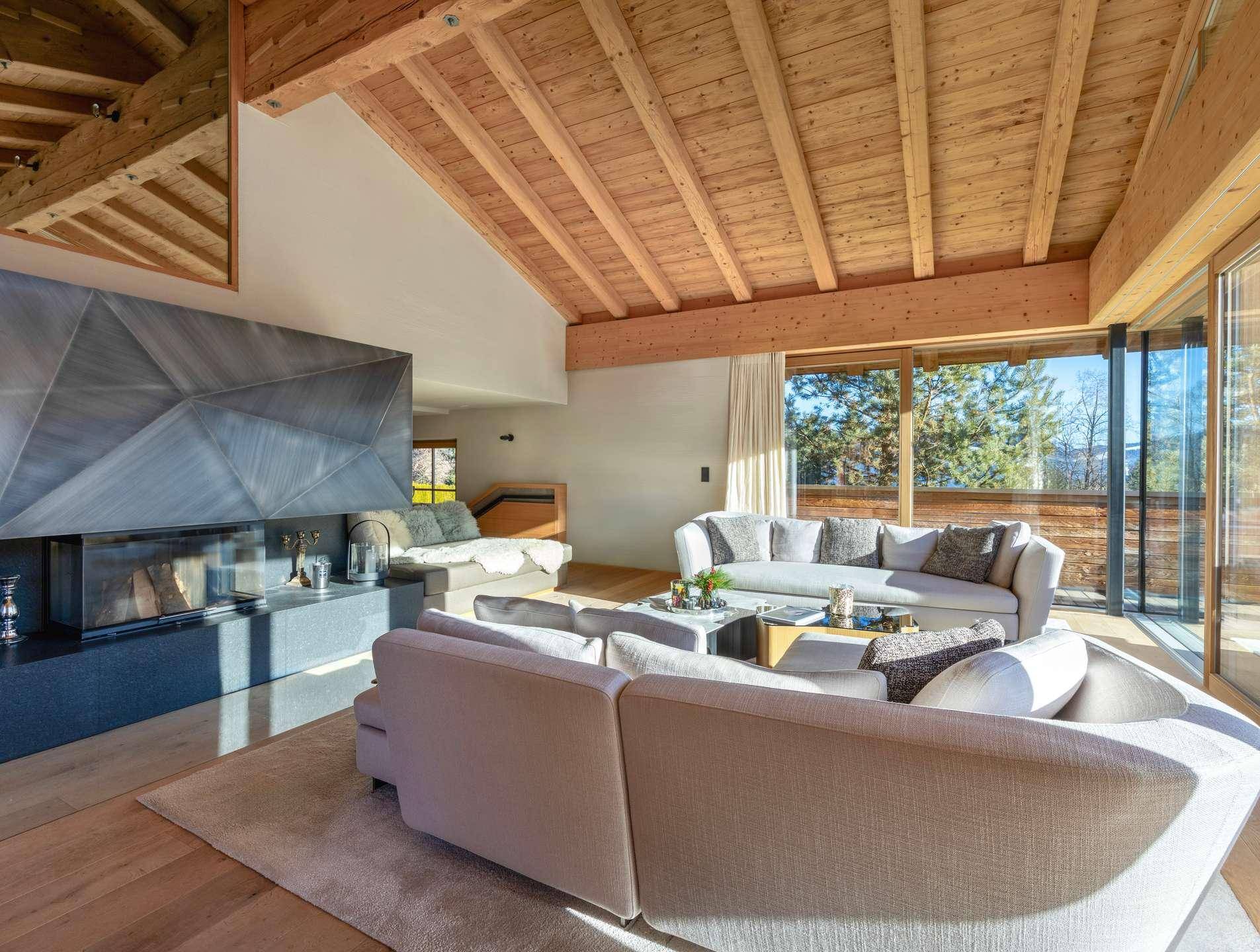 Helles Wohnzimmer mit modernem Kamin, Holzbalkendecke und großen Glasfronten zur Terrasse.