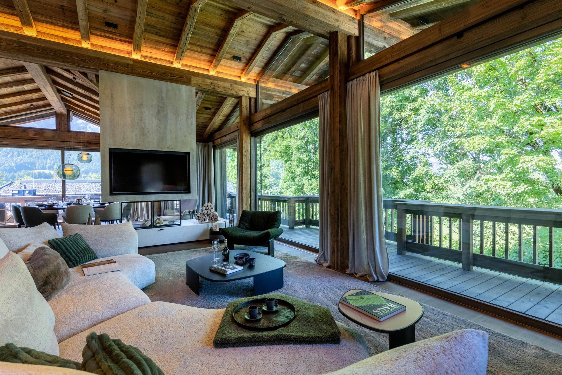 Geräumiges Wohnzimmer mit Holzbalkendecke, Kamin und großen Fenstern mit Blick ins Grüne.