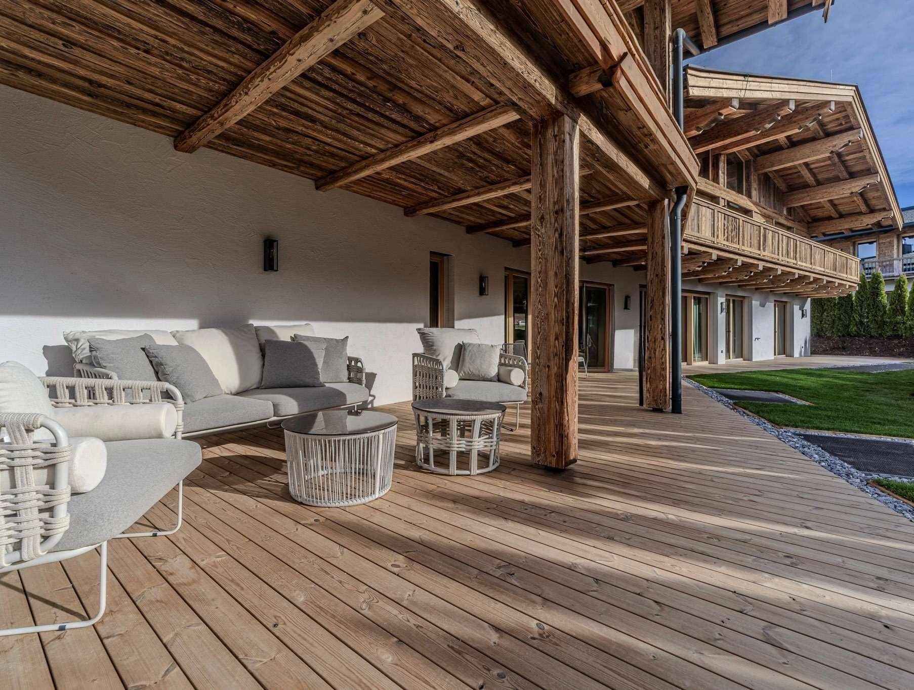 Große überdachte Holzterrasse mit bequemen Loungemöbeln und Blick auf den Garten.