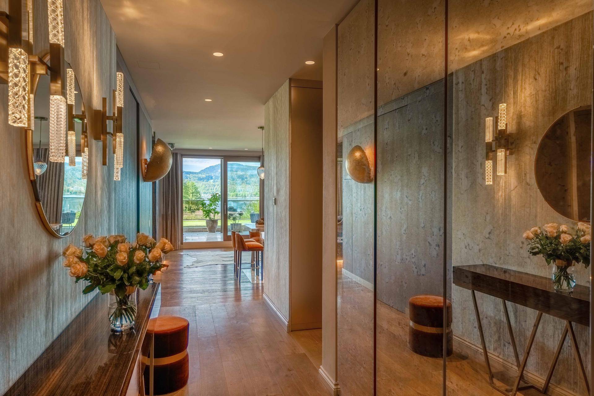 Heller Flur mit Spiegelfronten, eleganten Wandleuchten und einem Blick auf die umliegende Natur.