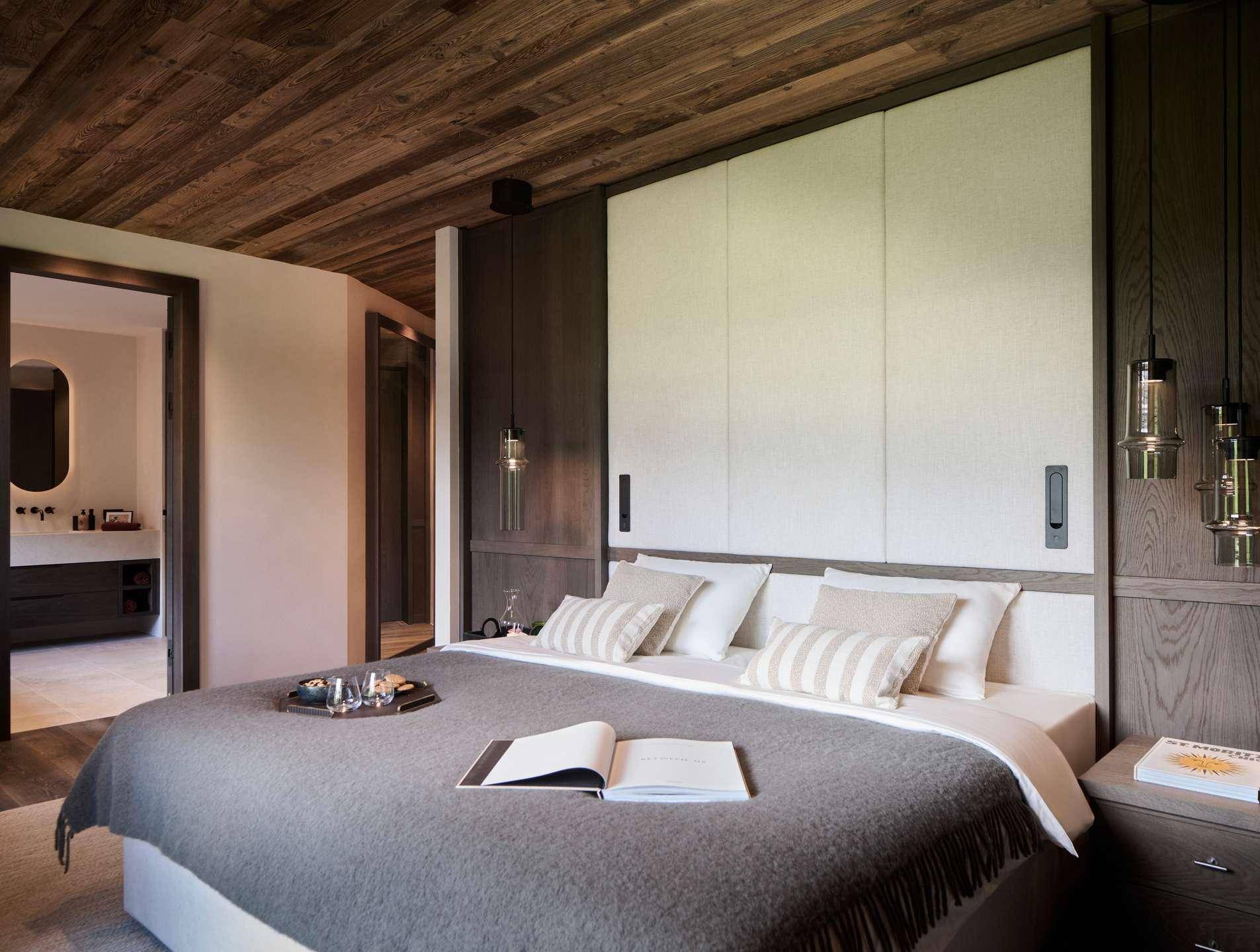 Gemütliches Schlafzimmer mit Holzbalkendecke, großem Bett und Zugang zu einem modernen Badezimmer.