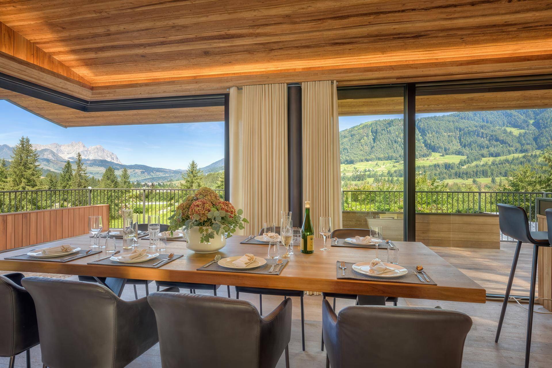 Eleganter Essbereich mit Holztisch und Stühlen, umgeben von großen Fenstern mit Bergblick.