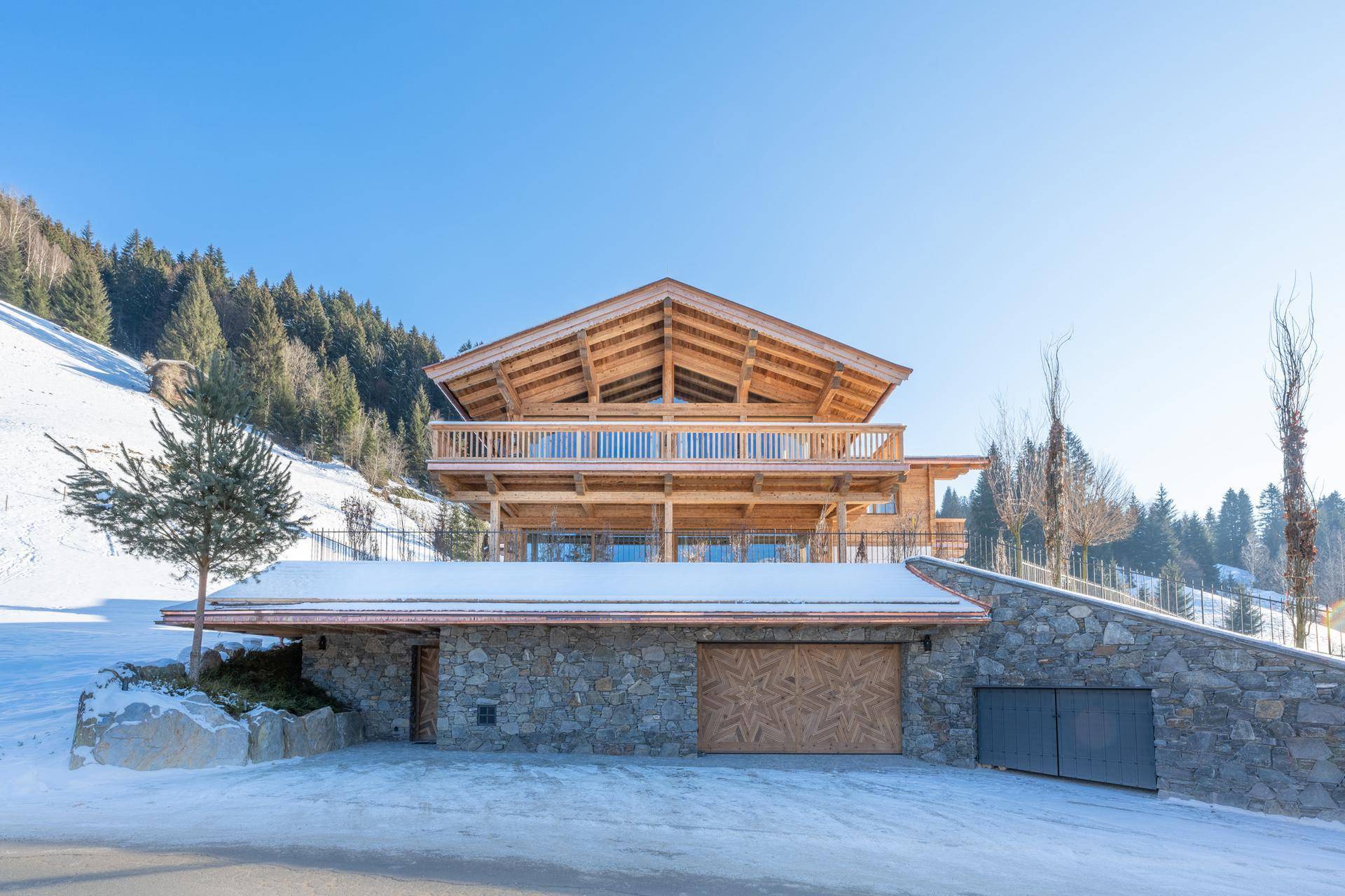 Beeindruckendes Chalet mit Steinfassade, Holzverkleidung und integrierter Garage in verschneiter Umgebung.