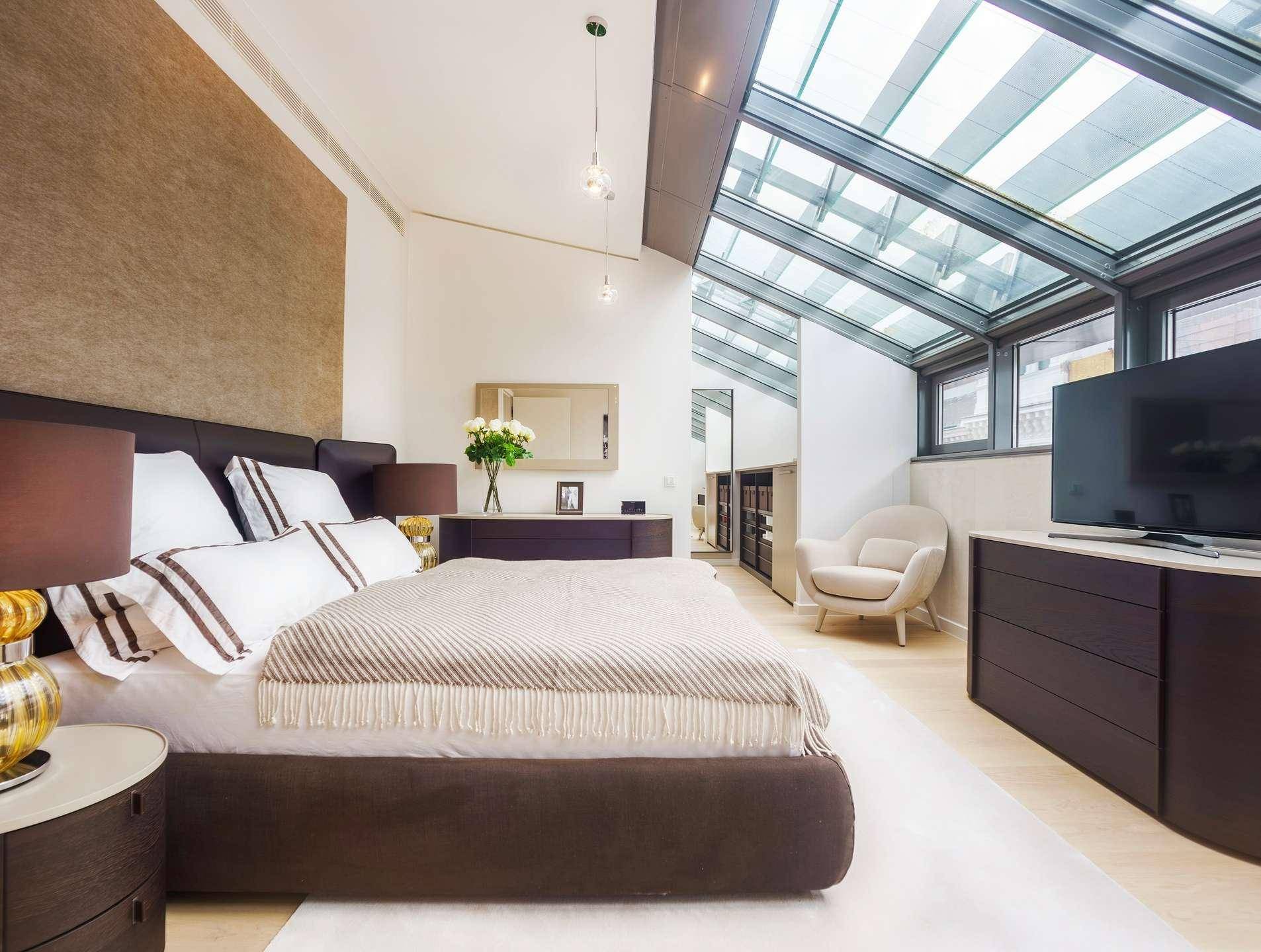 Modernes Schlafzimmer mit großem Bett, Holzboden und einem beeindruckenden Glasdach für viel Helligkeit.
