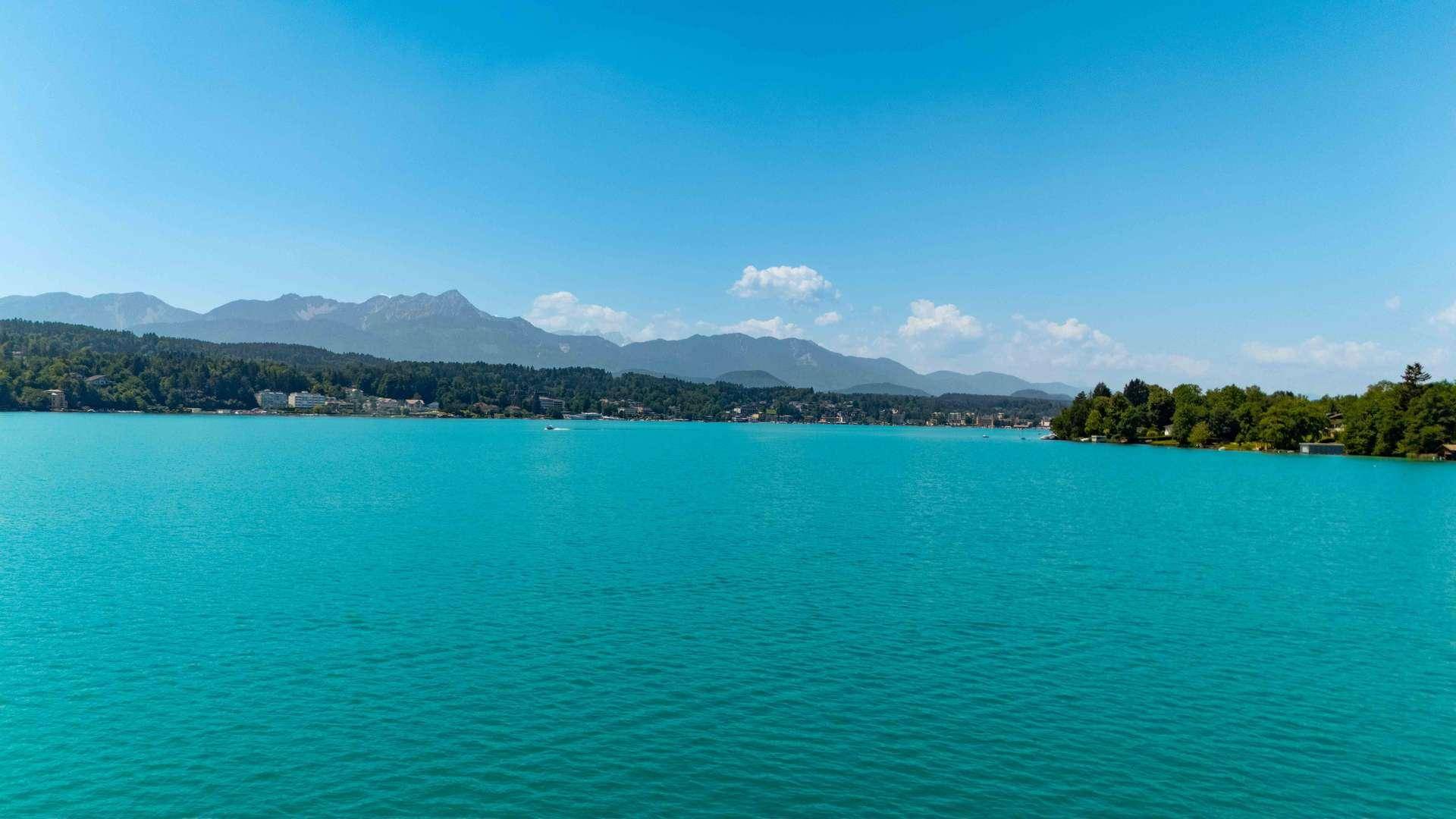 Weitläufiger Blick über den glitzernden See mit einer beeindruckenden Bergkulisse im Hintergrund.