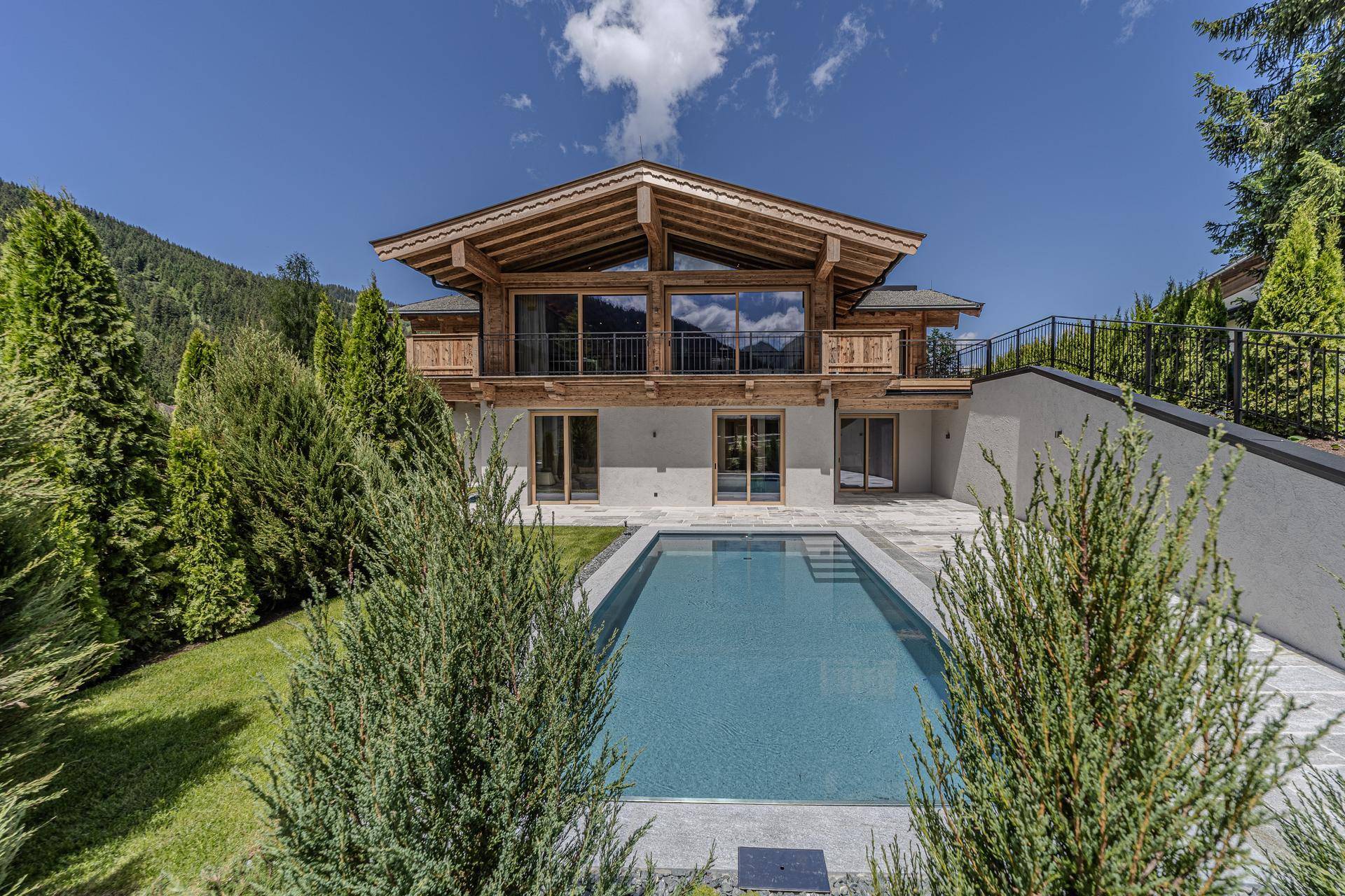 Luxuriöses Chalet mit Außenpool und gepflegter Gartenanlage unter blauem Himmel.