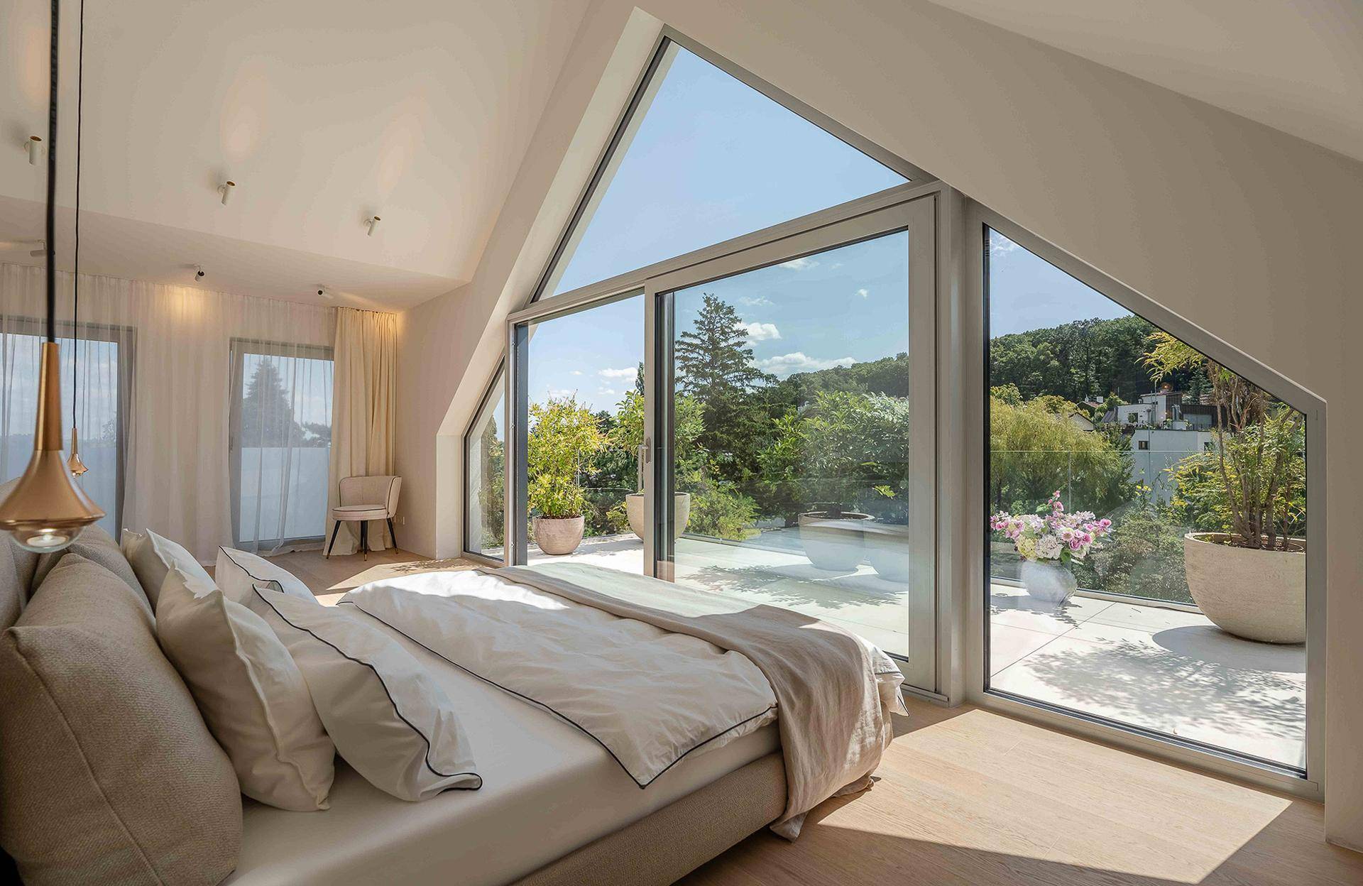 Helles Schlafzimmer im Dachgeschoss mit großen Fenstern, Holzboden und Zugang zur Dachterrasse.
