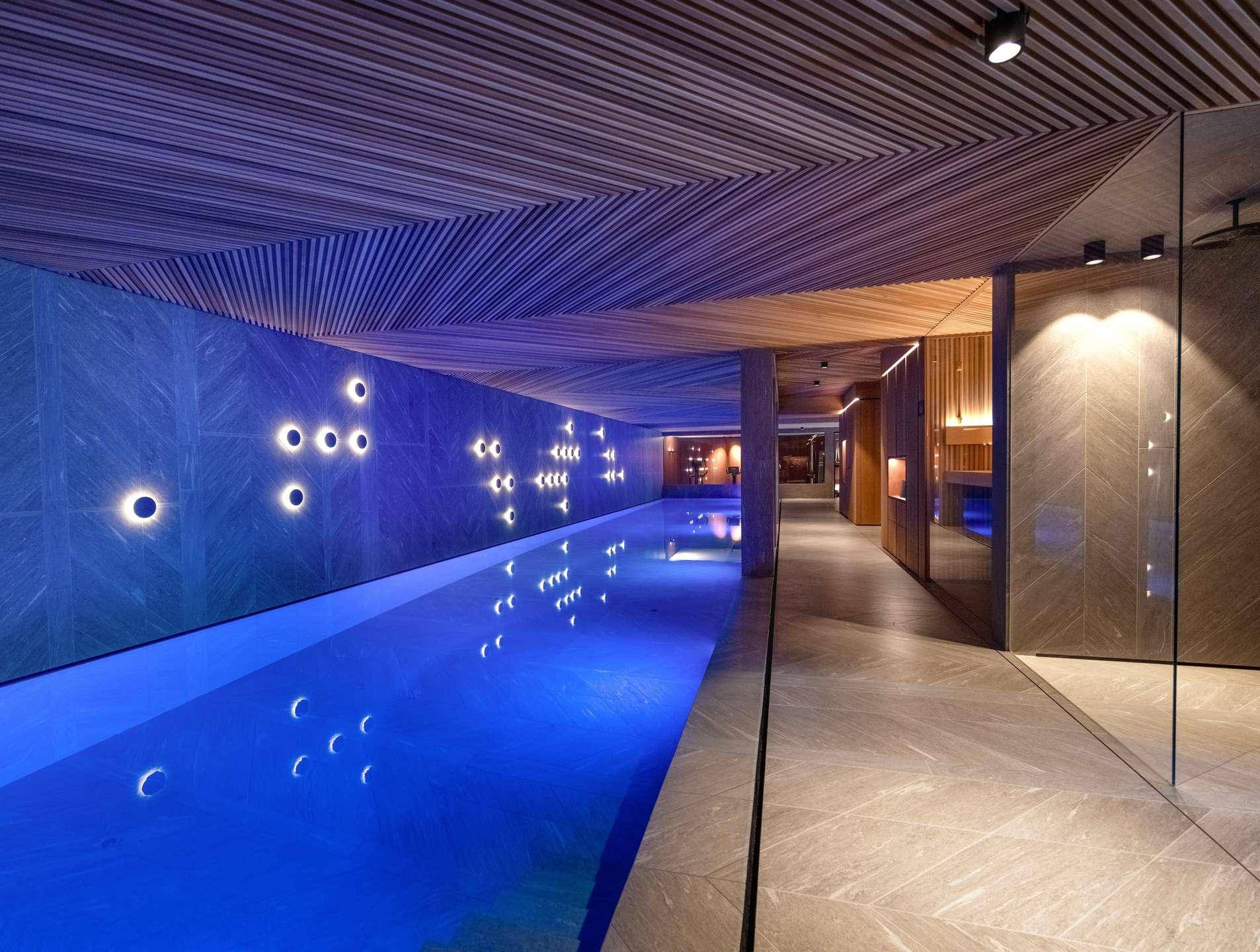 Beeindruckender Innenpool mit blauer Beleuchtung, Holzdecke und Wellnessbereich.