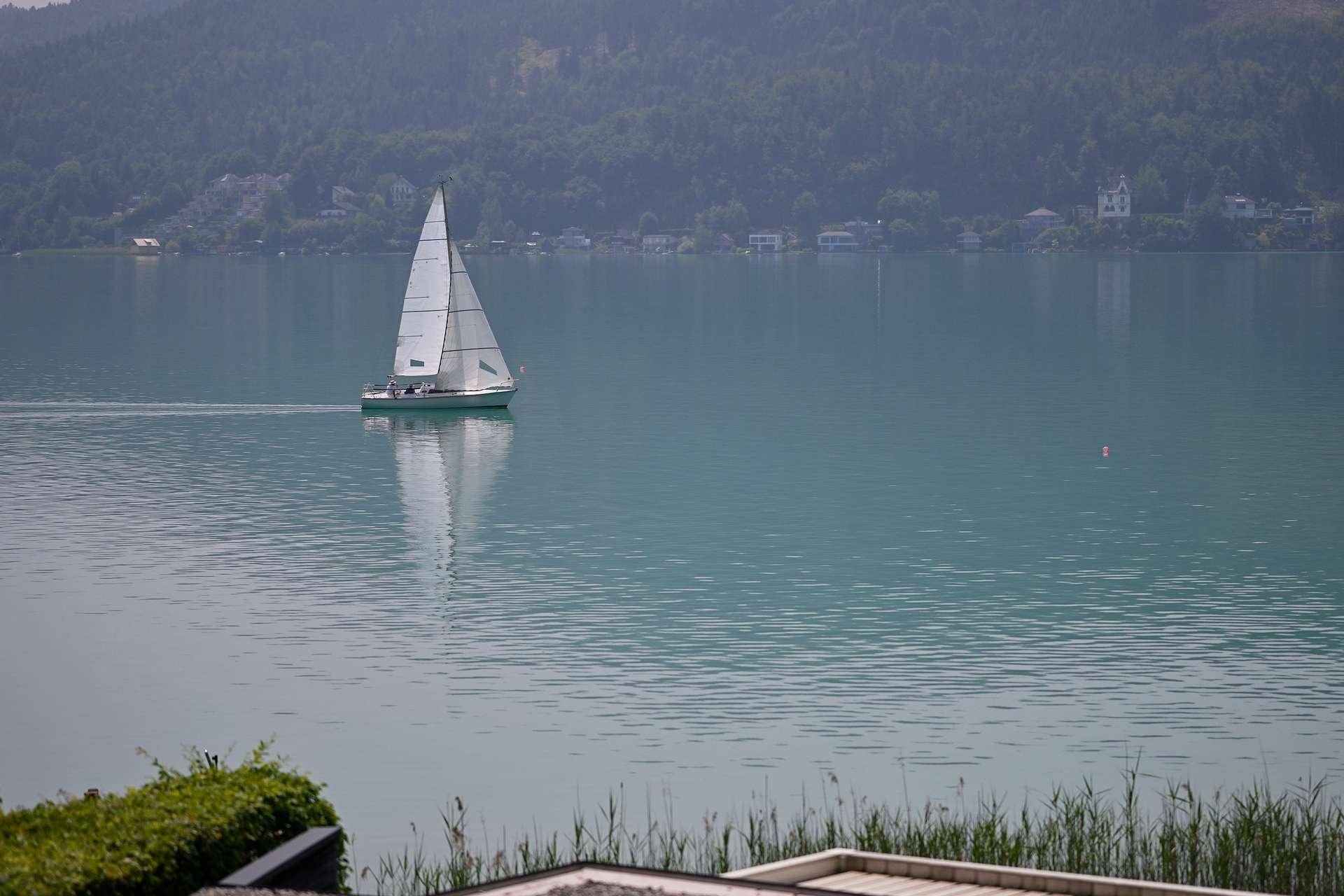 Segelboot auf dem ruhigen See mit bewaldeten Bergen im Hintergrund, eine idyllische Aussicht.