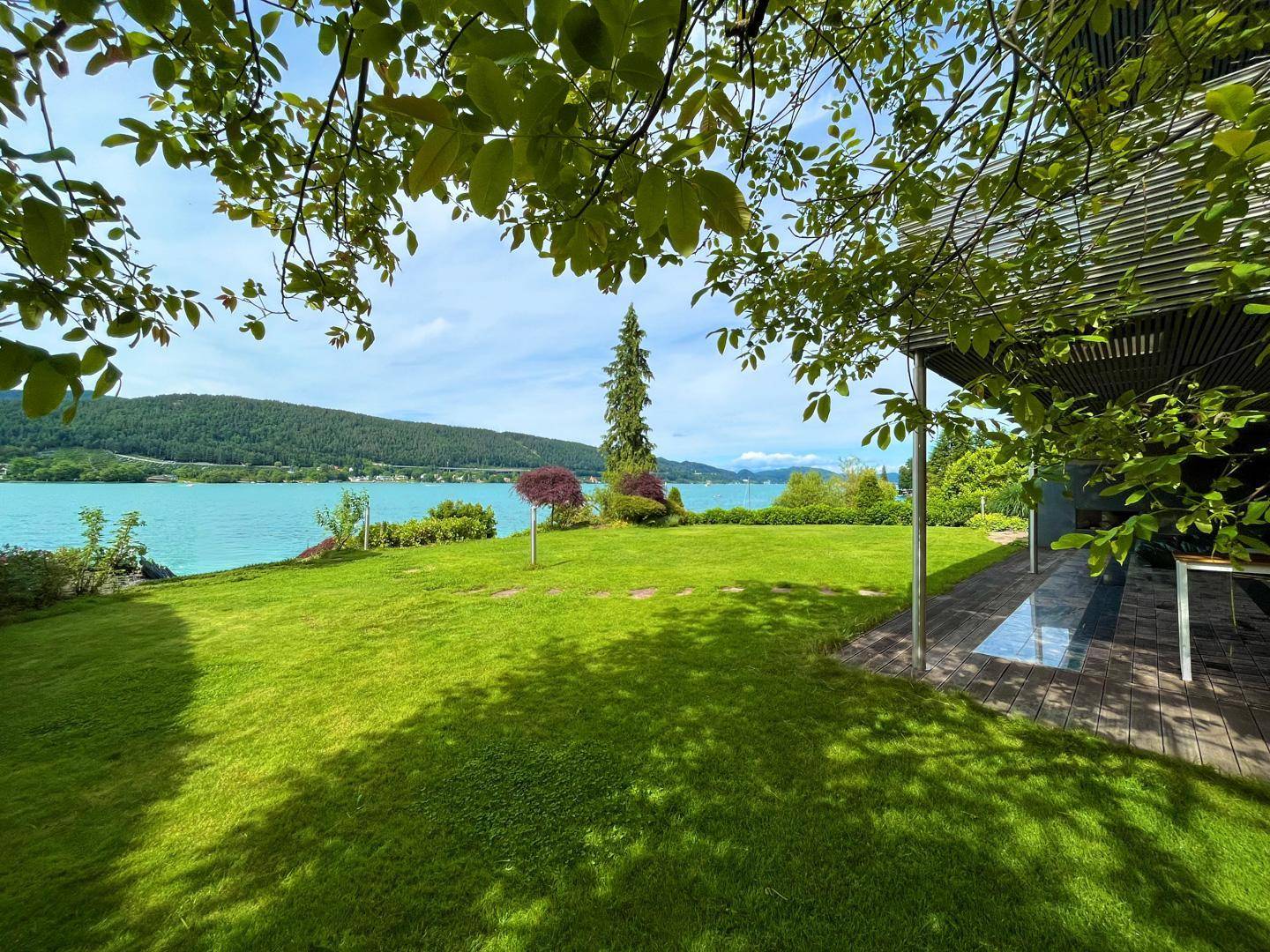 Idyllischer Gartenbereich mit direktem Zugang zum See, umgeben von üppigem Grün und moderner Architektur.