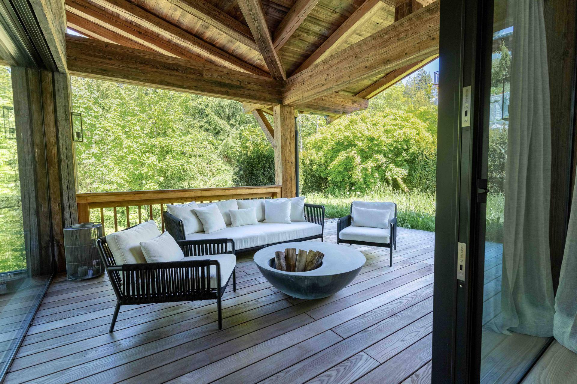 Überdachte Terrasse mit bequemen Loungemöbeln und Blick auf die grüne Waldlandschaft.