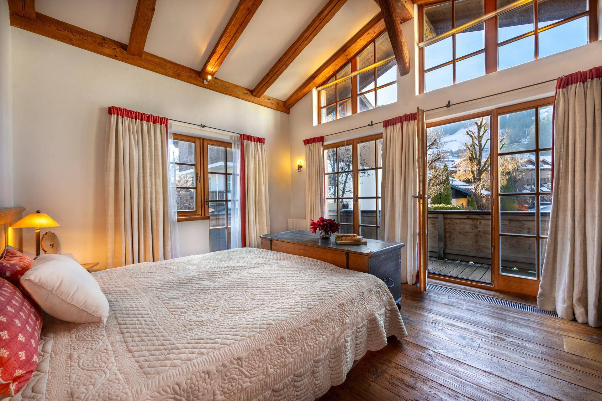 Helles Schlafzimmer mit hohen Decken, Holzbalken und Zugang zu einem Balkon mit Bergblick.