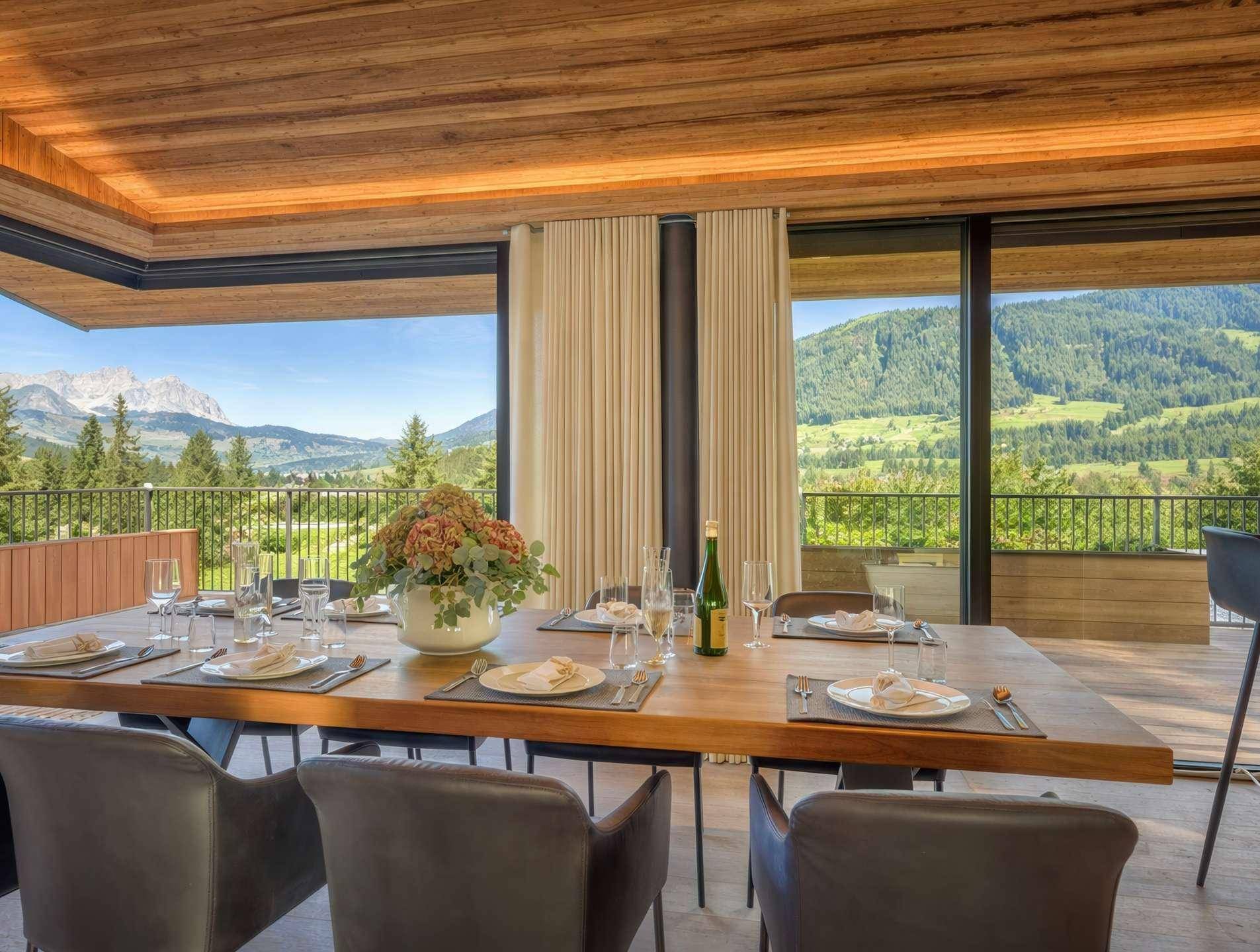 Eleganter Essbereich mit Holztisch und Stühlen, umgeben von Panoramafenstern mit Bergblick.