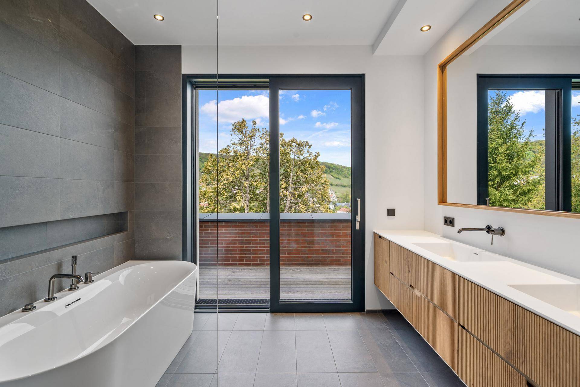 Modernes Badezimmer mit freistehender Badewanne, Doppelwaschbecken und Zugang zu einer Außenterrasse.
