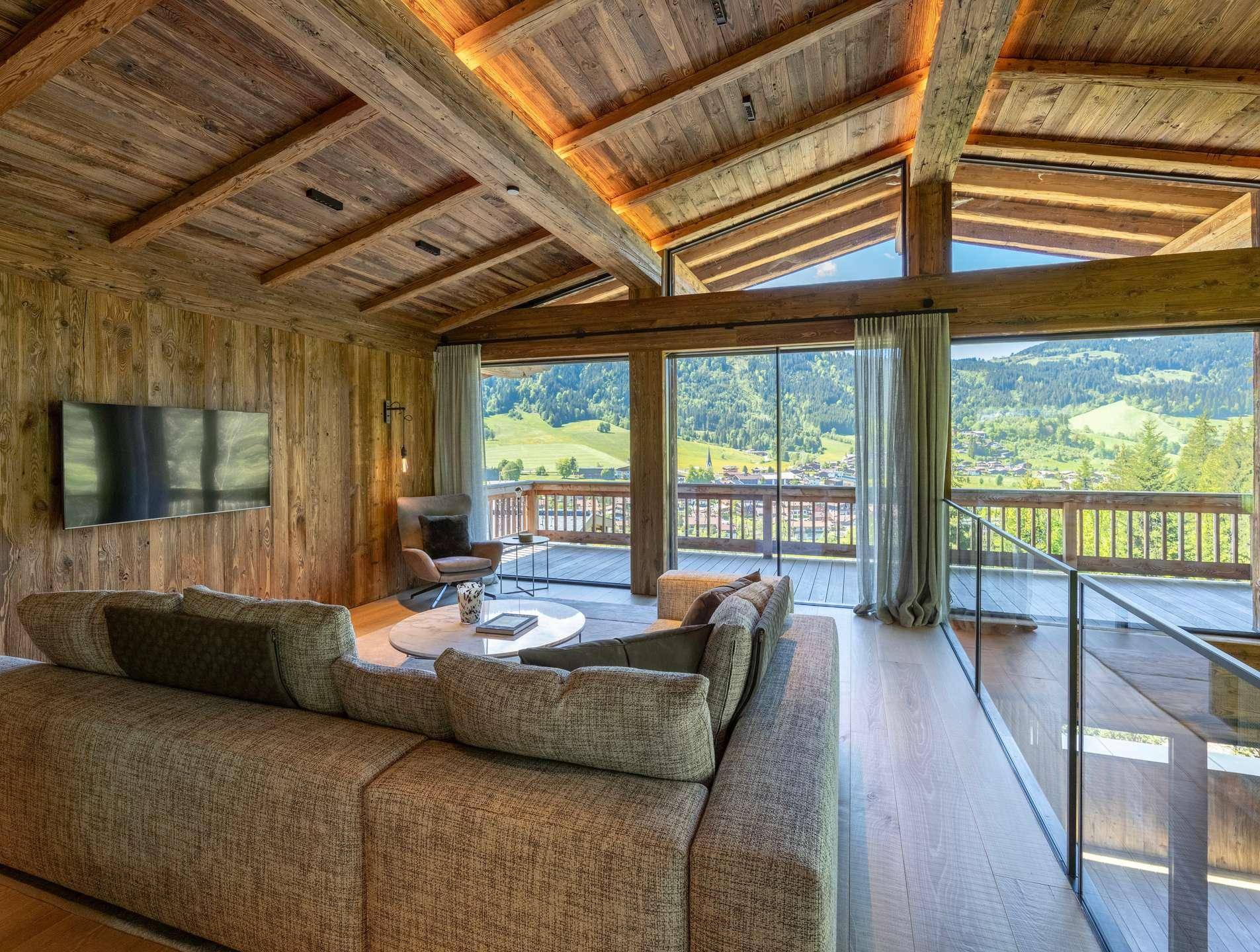 Gemütliches Wohnzimmer mit Holzwänden, großem Sofa und weitem Blick auf die grüne Landschaft.