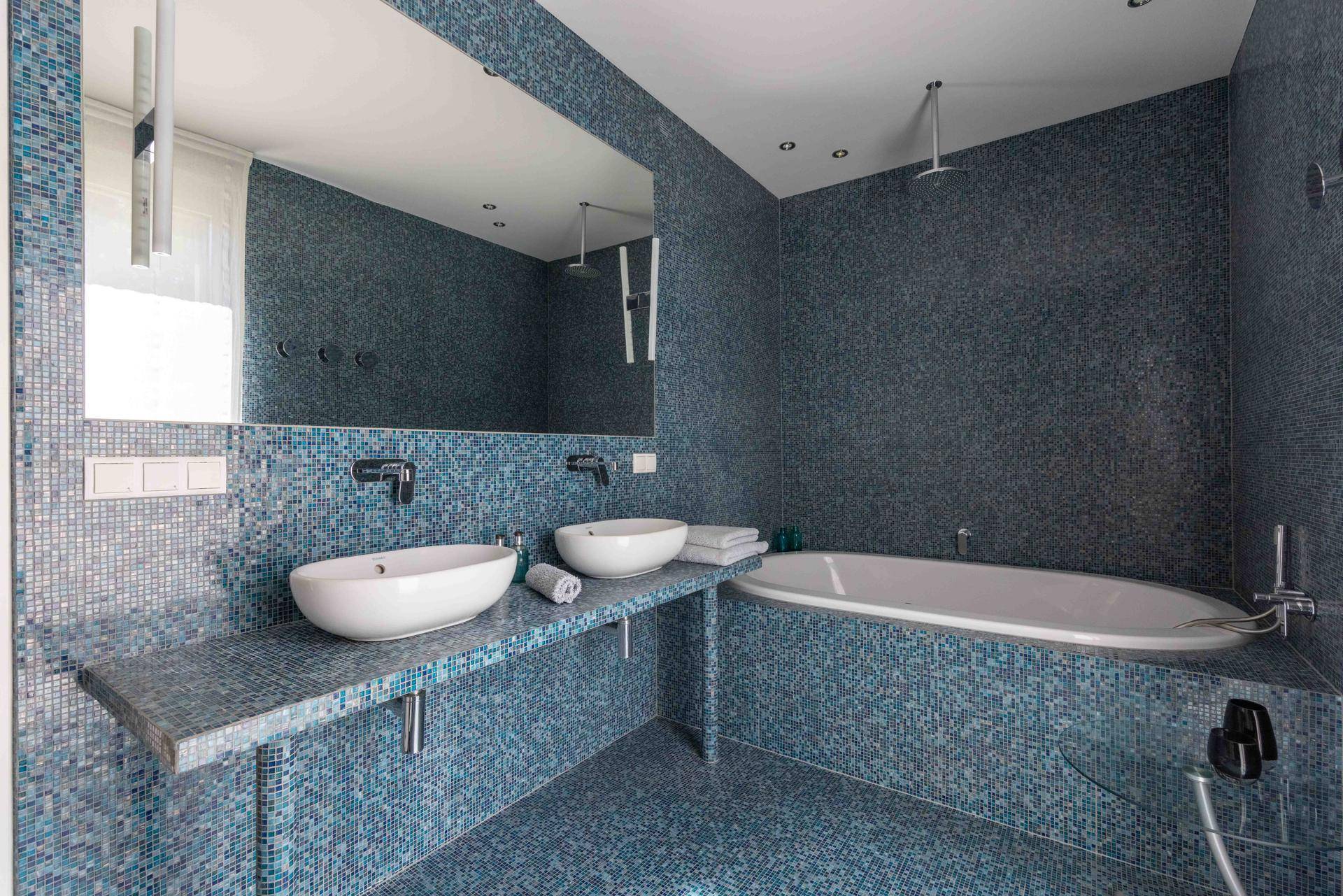 Modernes Badezimmer mit blauen Mosaikfliesen, Doppelwaschbecken und integrierter Badewanne.