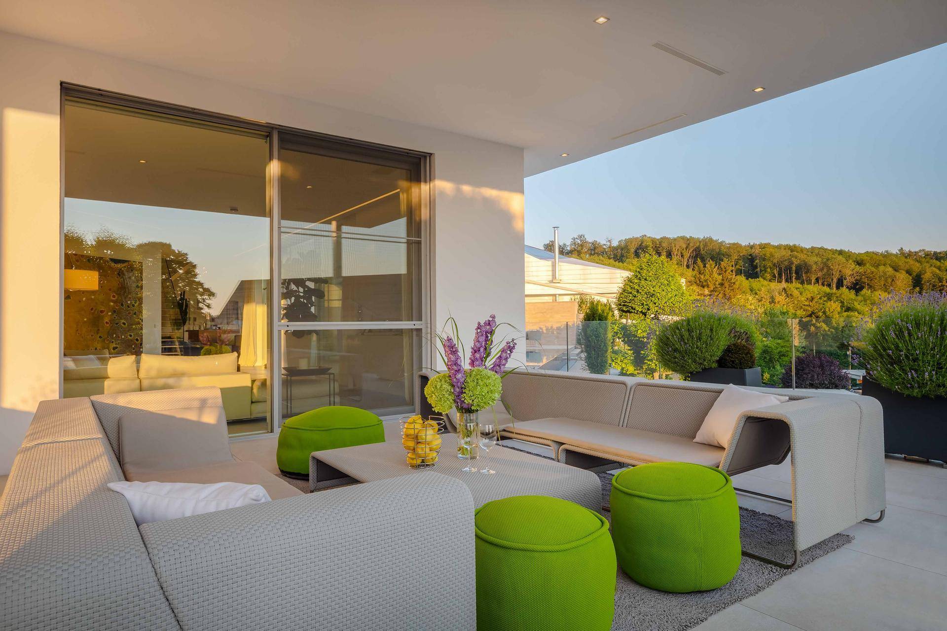 Stilvolle Lounge-Terrasse mit modernen Sofas und grünen Akzenten, bietet einen entspannenden Blick ins Grüne.
