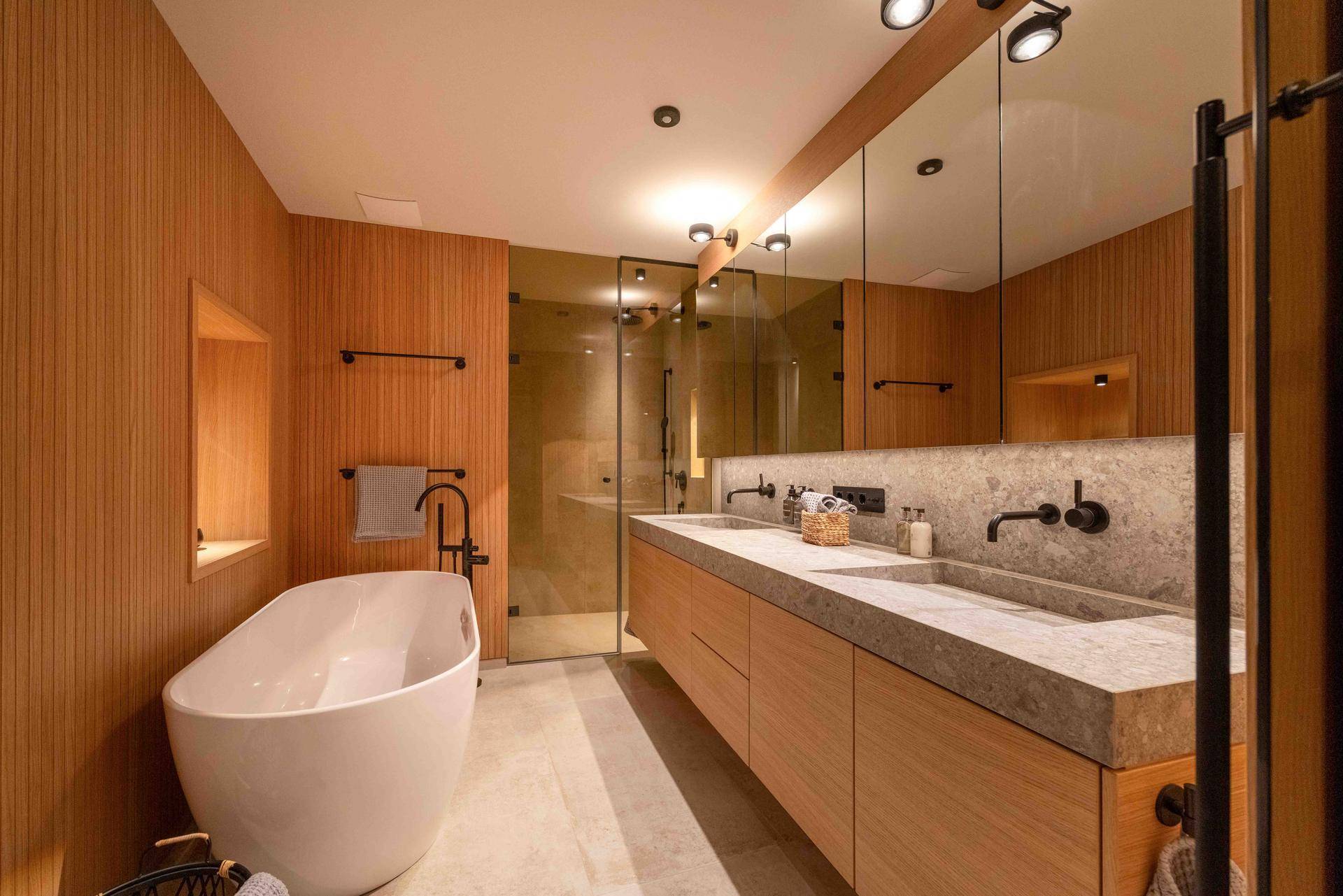 Modernes Badezimmer mit freistehender Badewanne, Doppelwaschbecken und Holzverkleidung.