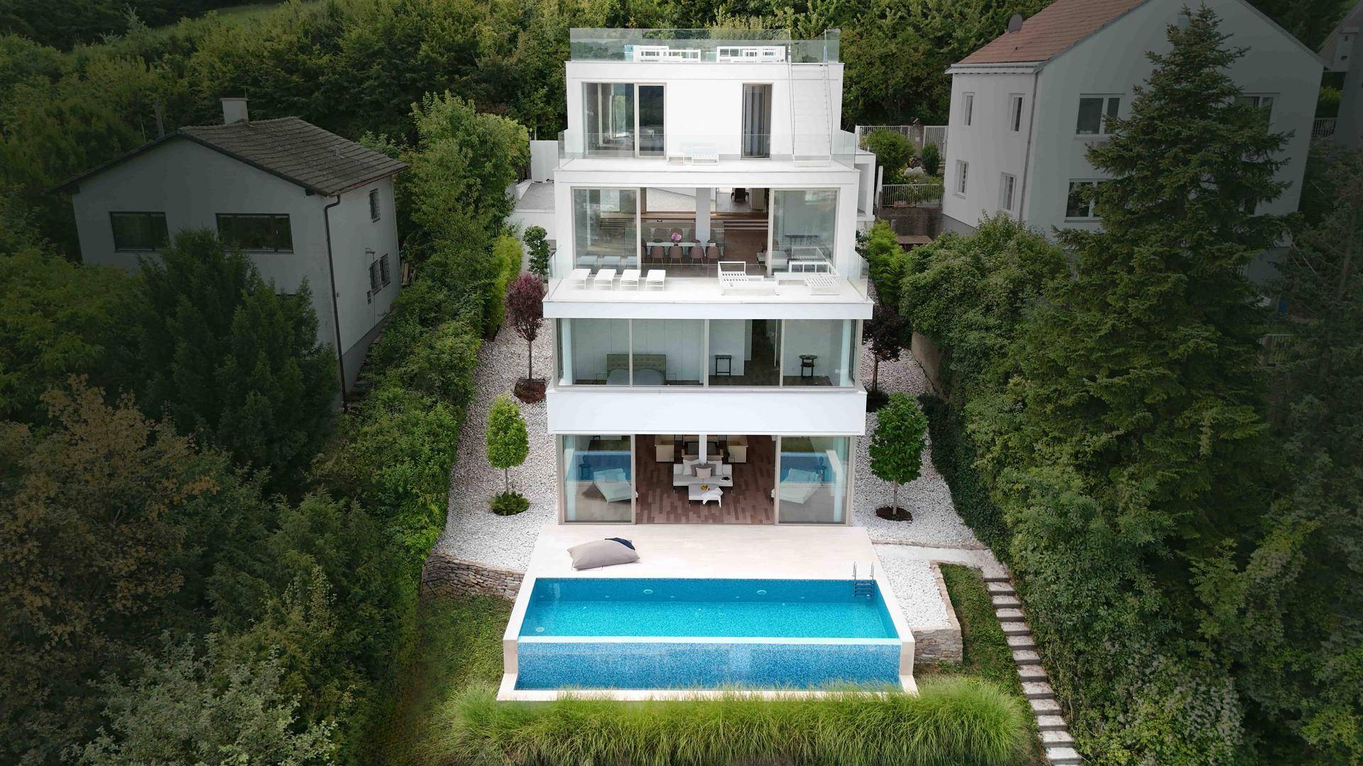 Moderne Villa mit mehreren Terrassen, großem Pool und umgeben von üppigem Grün in Hanglage.