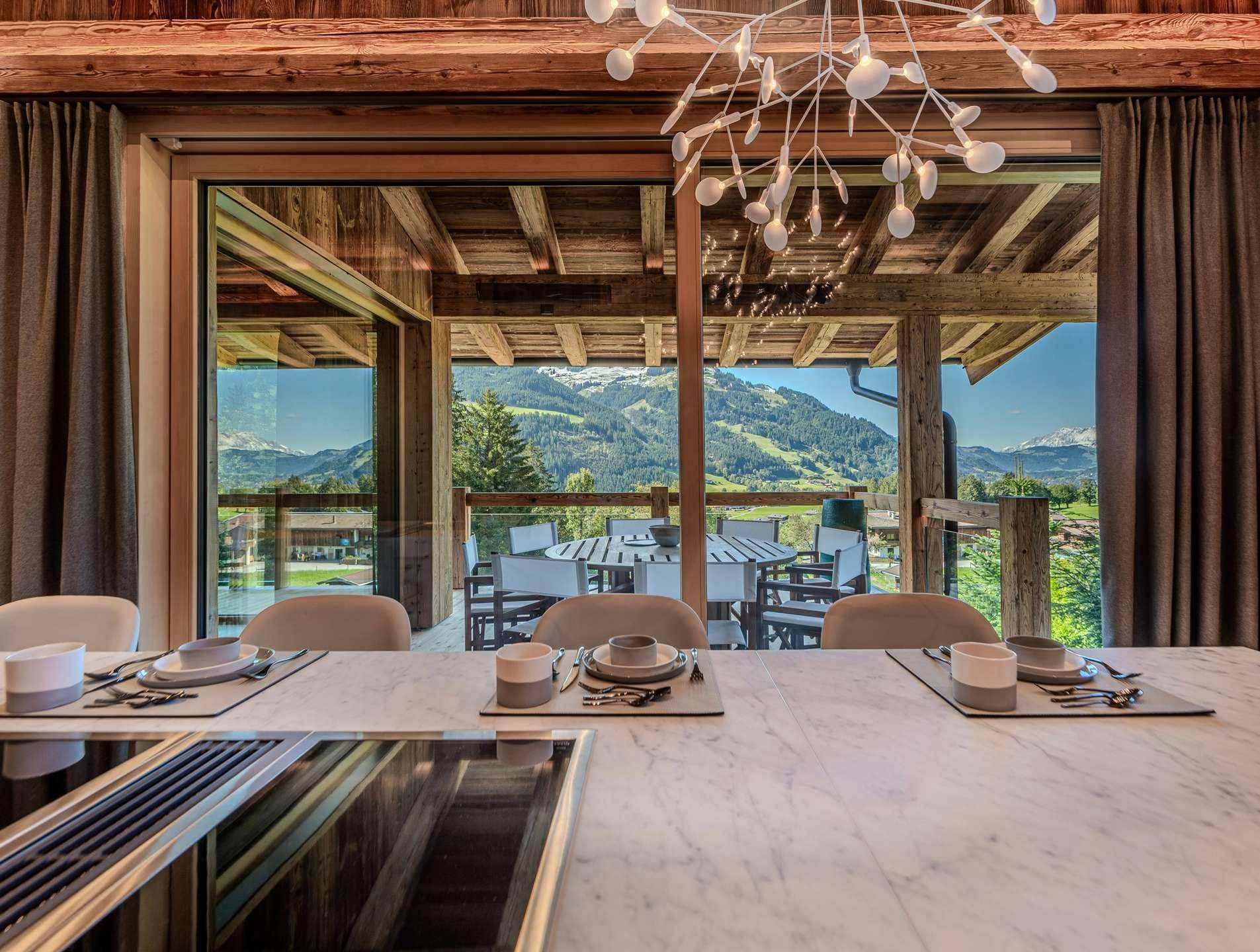 Moderne Küche mit Marmorarbeitsplatte und Essbereich, der auf einen Balkon mit Bergblick führt.
