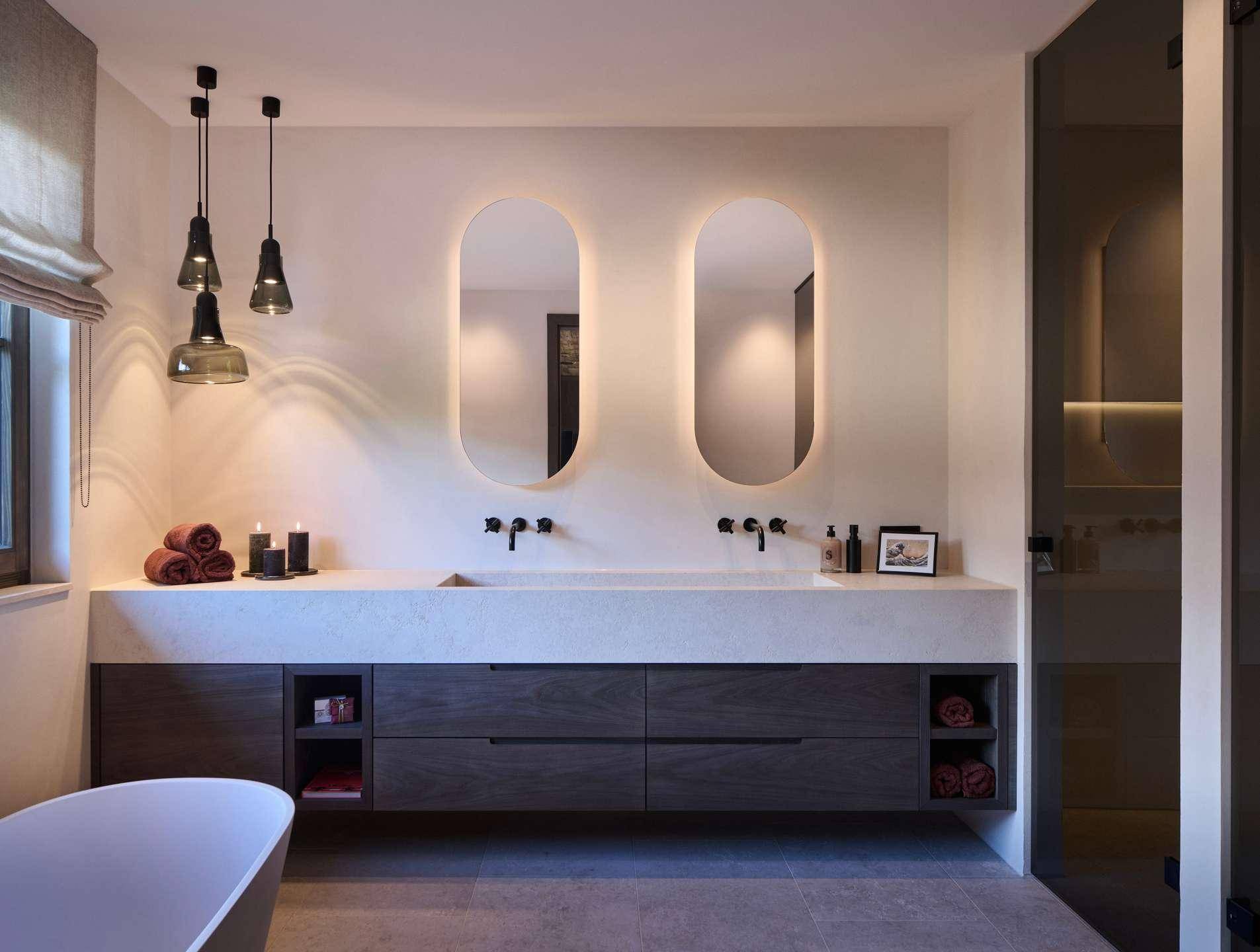 Modernes Badezimmer mit Doppelwaschbecken, beleuchteten Spiegeln und freistehender Badewanne.