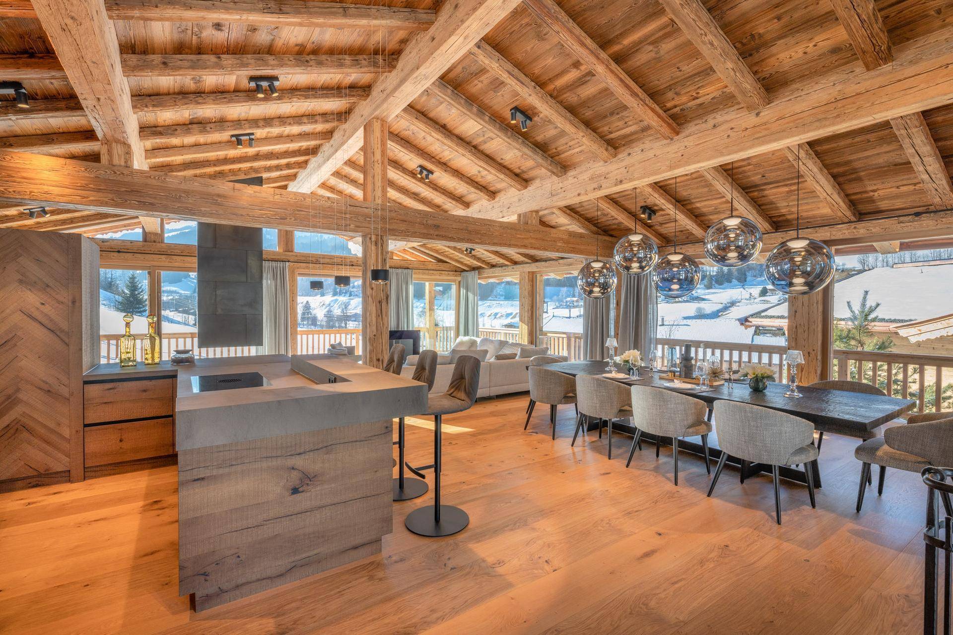 Offener Wohnbereich mit Küche, Essbereich und gemütlicher Sitzecke, umgeben von Holz und Bergblick.