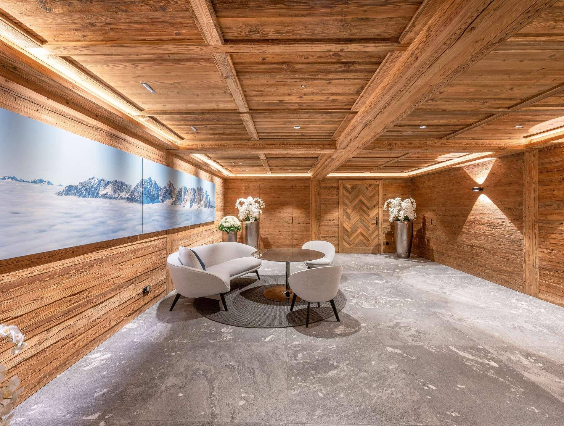 Stilvoller Loungebereich mit Holzwänden, Steinfliesen und einem großen Wandbild, das eine Berglandschaft zeigt.