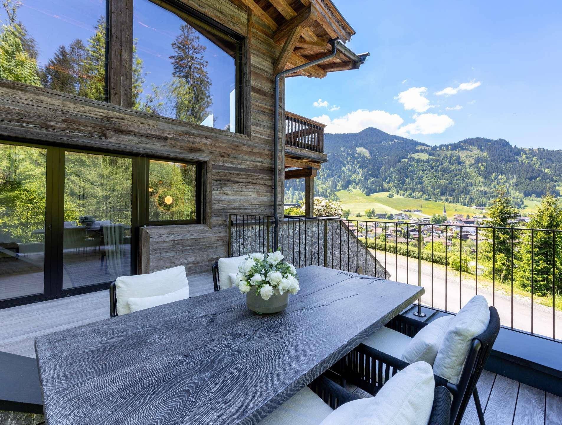Großer Balkon mit Esstisch und Stühlen, umgeben von einer malerischen Berglandschaft.