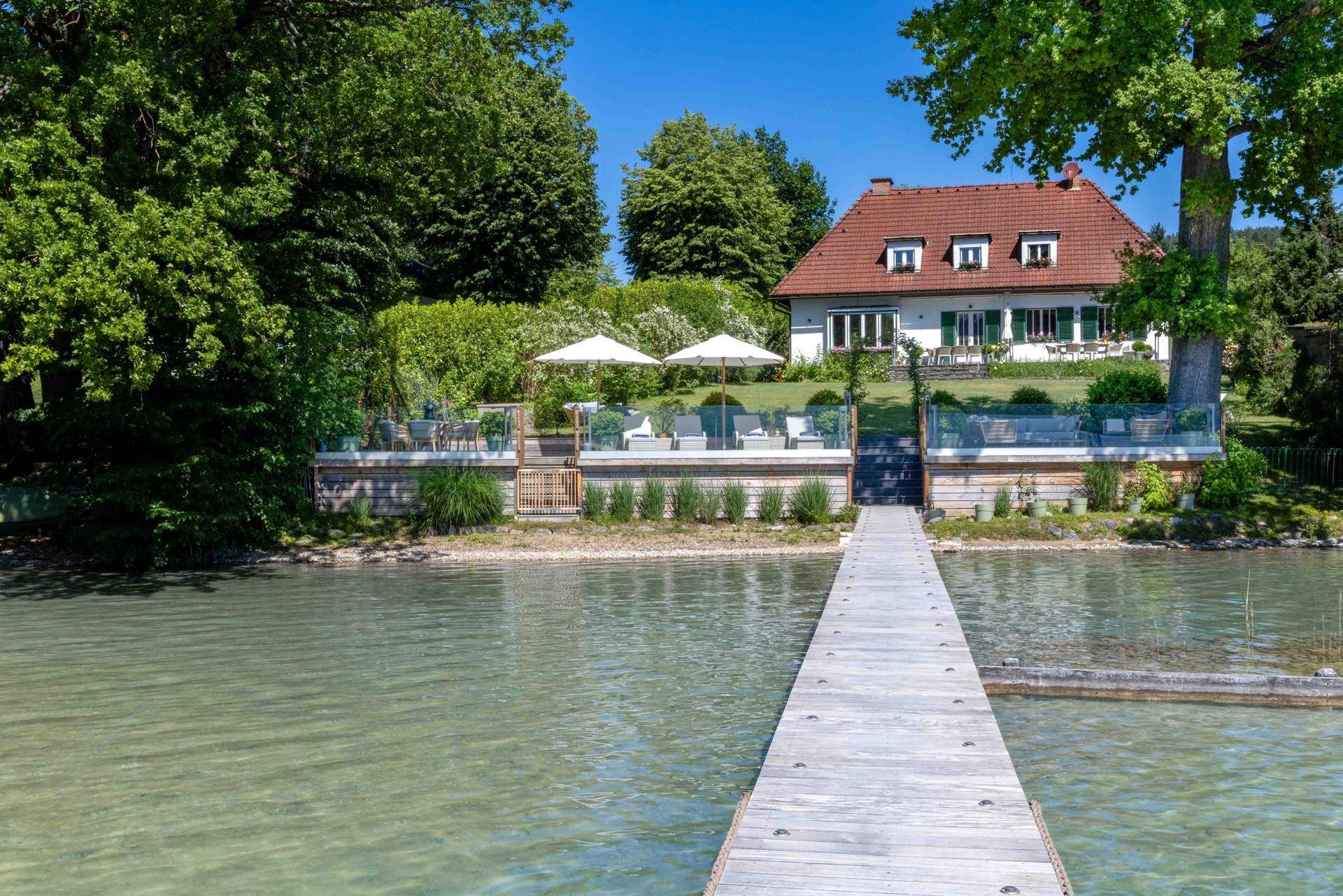 Charmantes Haus mit rotem Dach und Seeblick, verbunden durch einen Holzsteg mit der Uferterrasse.