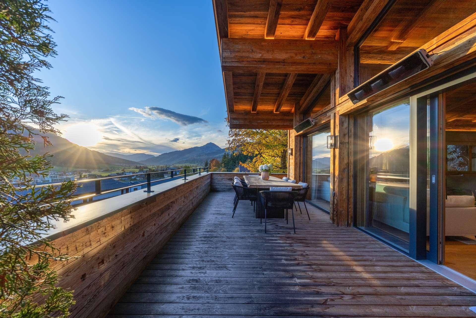 Geräumige Holzterrasse mit Esstisch und Stühlen, bietet einen weiten Blick auf die umliegende Berglandschaft.