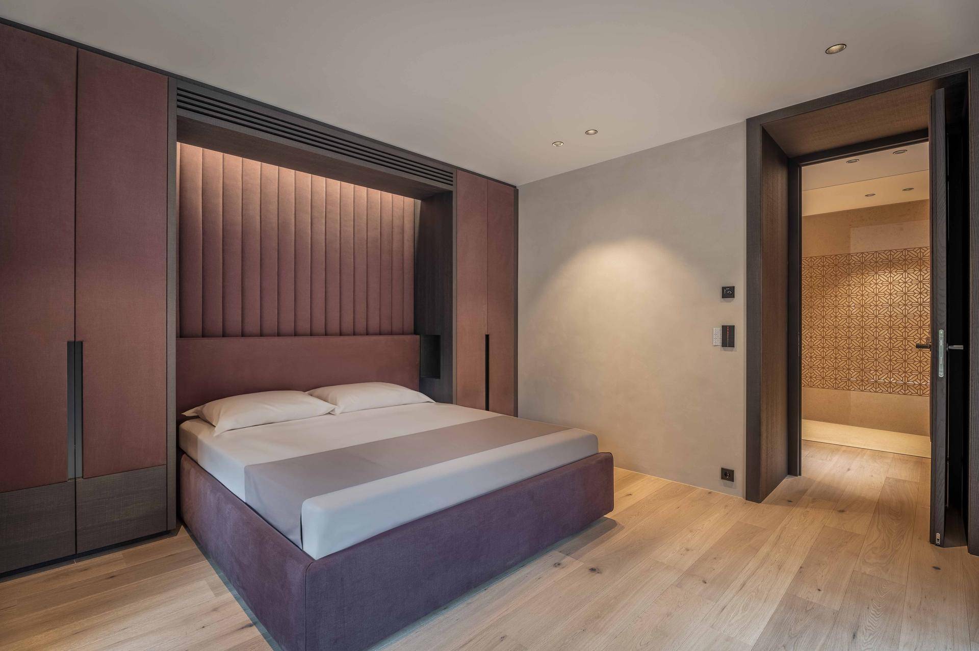 Modernes Schlafzimmer mit integrierten Schränken, gepolstertem Kopfteil und direktem Zugang zum Badezimmer.