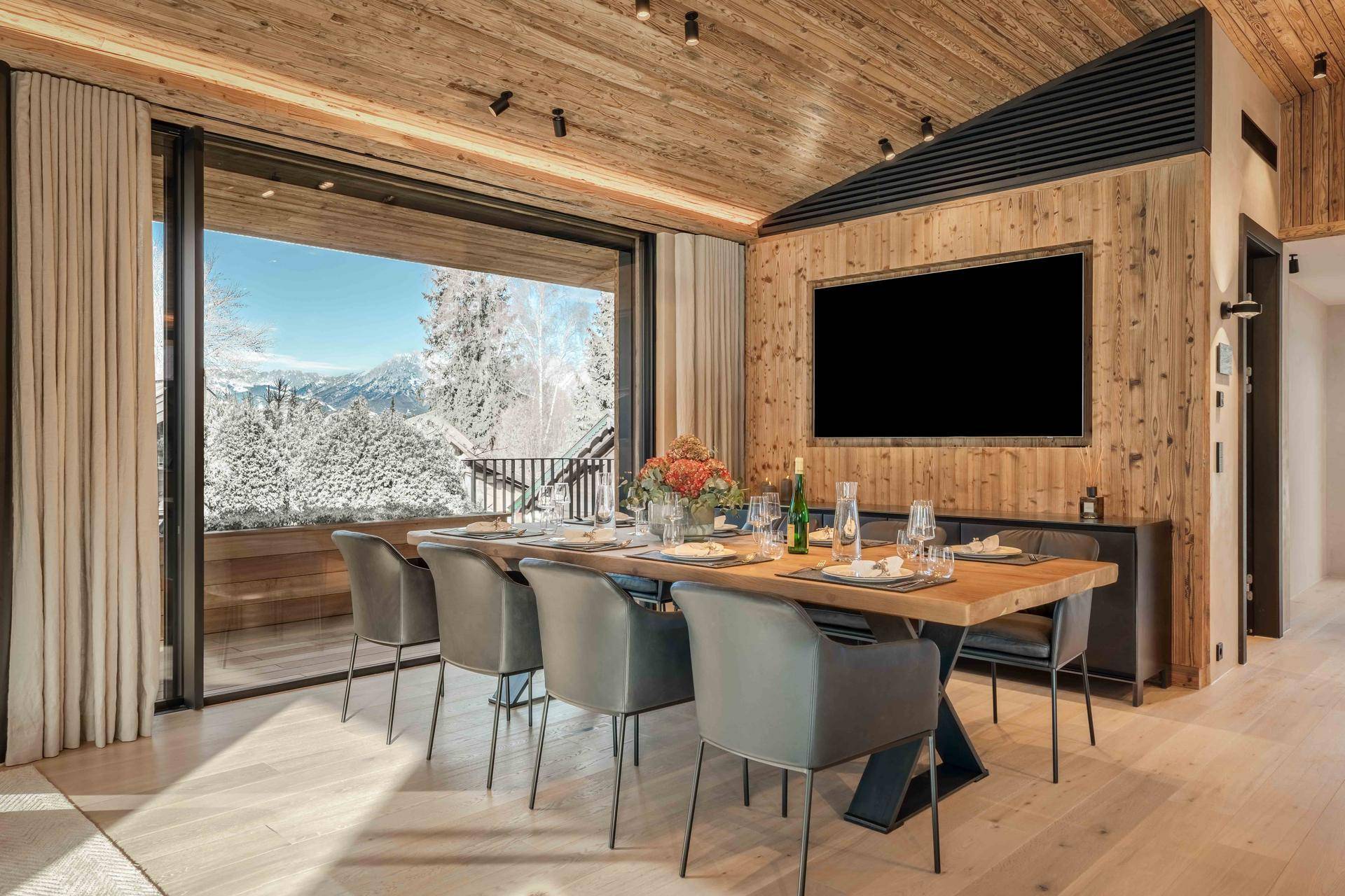 Eleganter Essbereich mit großem Holztisch, modernen Stühlen und Panoramablick auf die verschneiten Berge.
