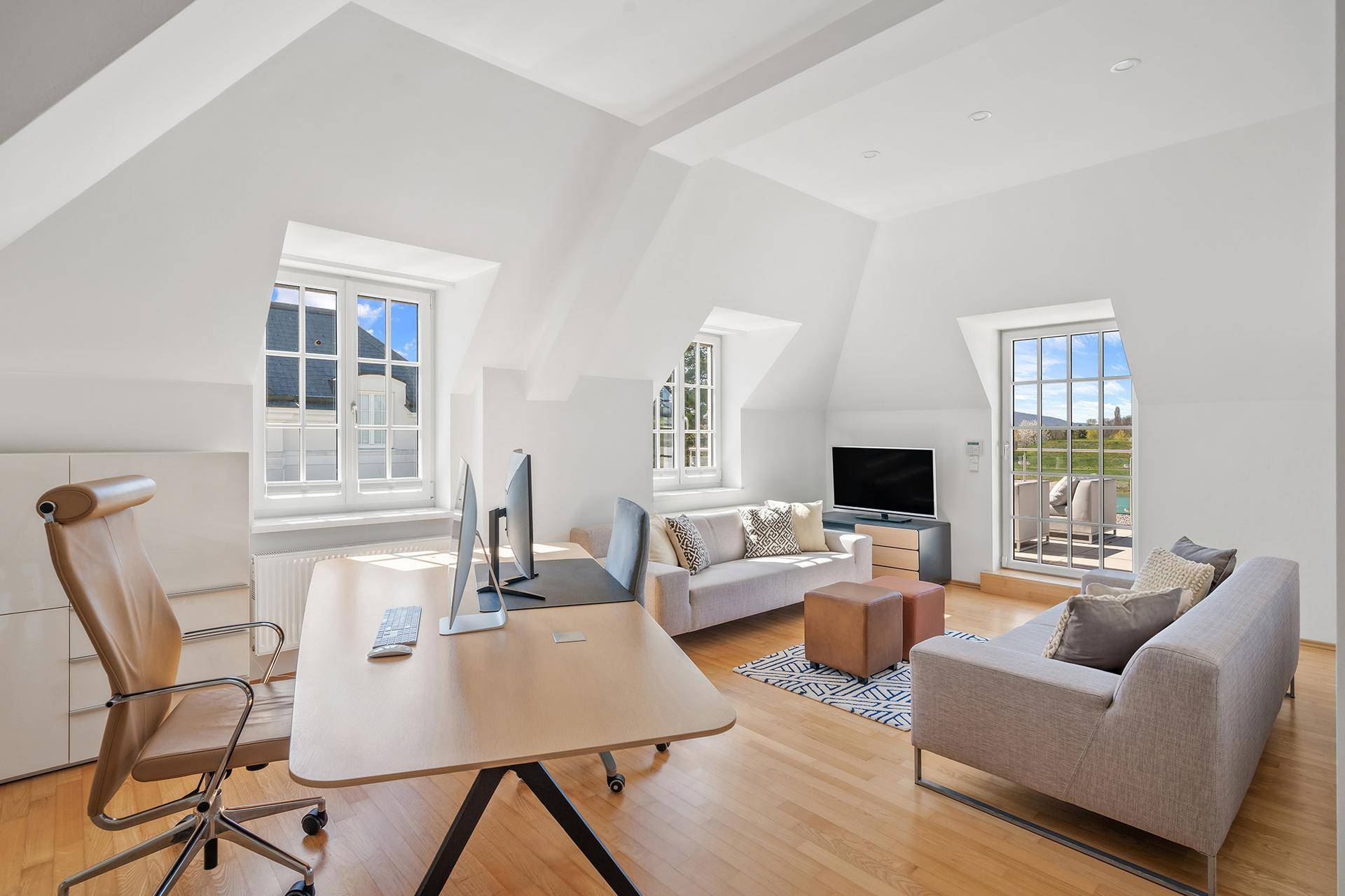 Helles Büro im Dachgeschoss mit Holzboden, Schreibtisch und gemütlicher Sitzecke mit Ausblick.