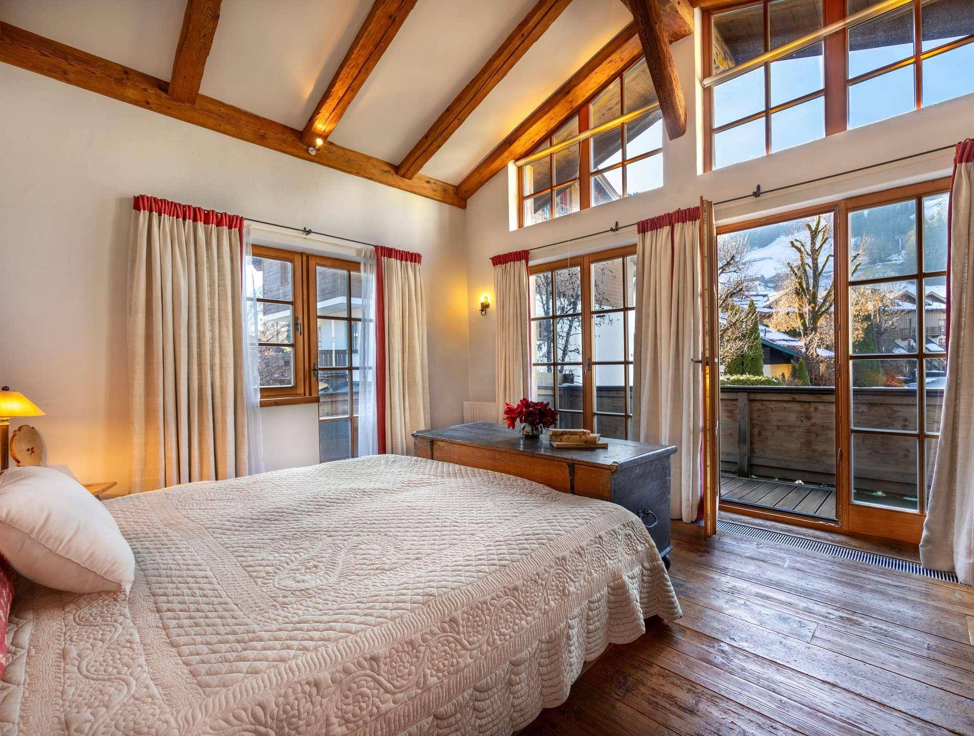 Geräumiges Schlafzimmer mit hohen Decken, Holzbalken und Zugang zu einem Balkon.