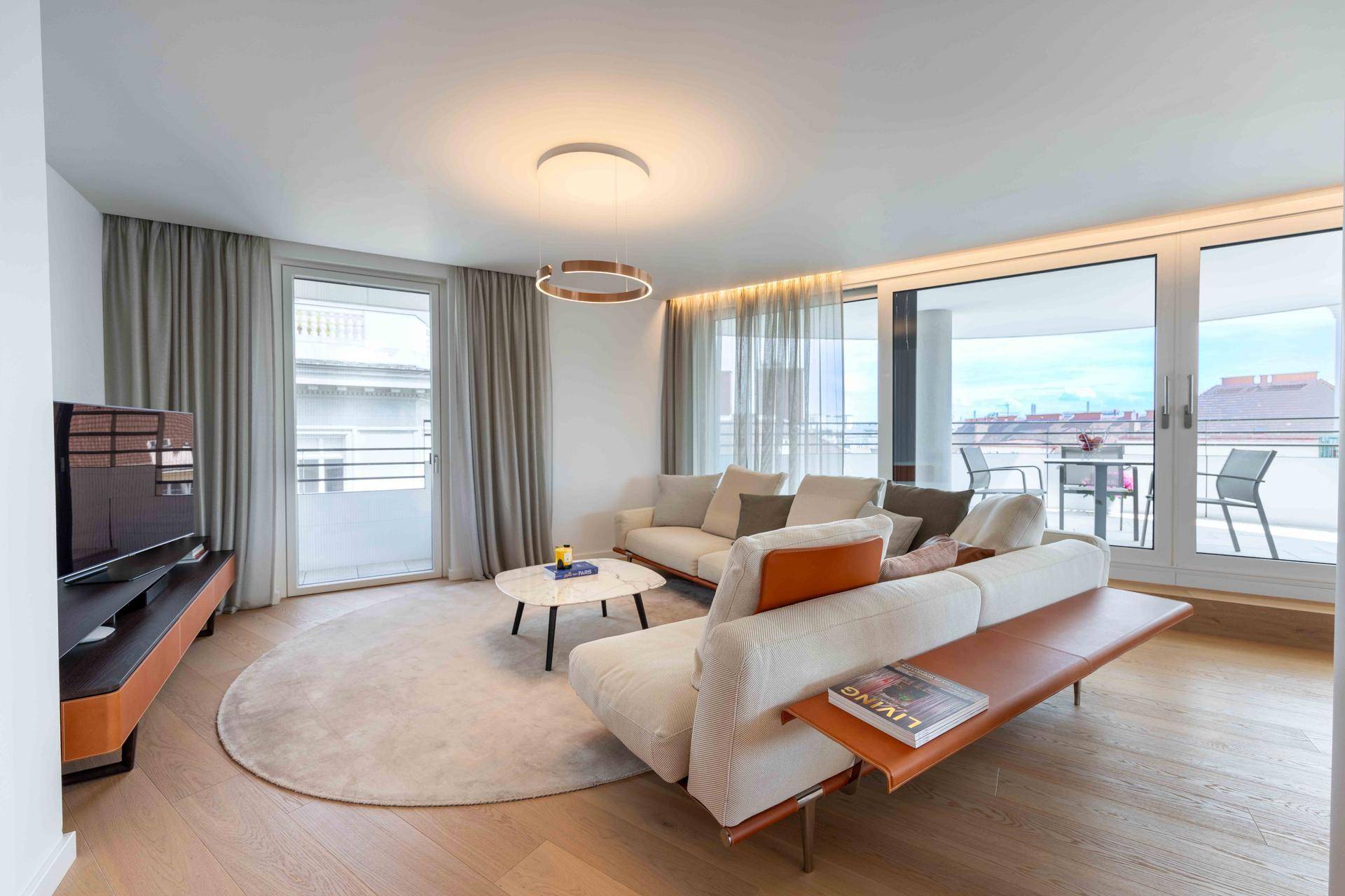 Gemütliches Wohnzimmer mit beiger Couch, Holzboden und großen Fenstern mit Stadtblick.